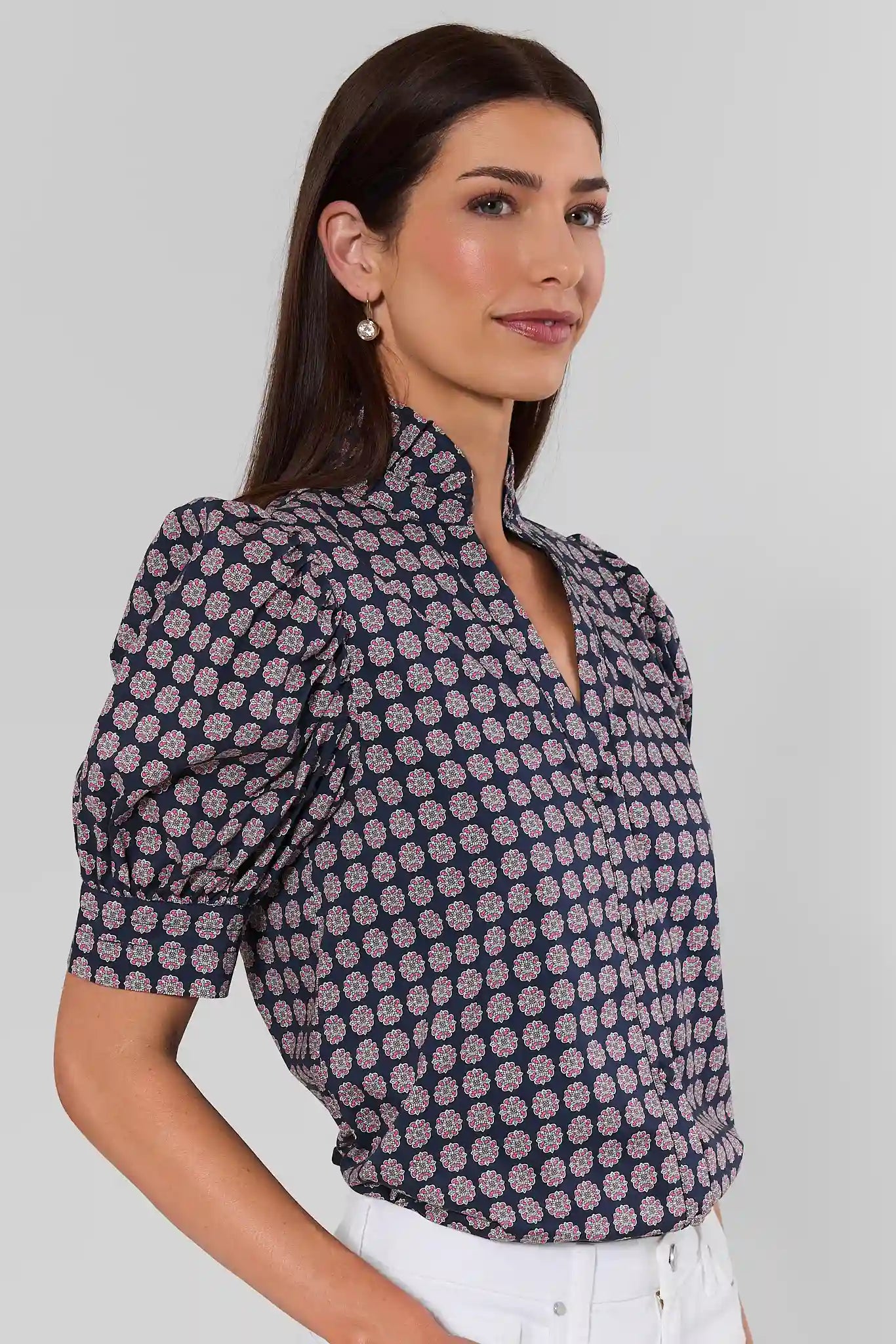 Woman standing to the side wearing a geometric navy and purple top with white jeans on a cream background