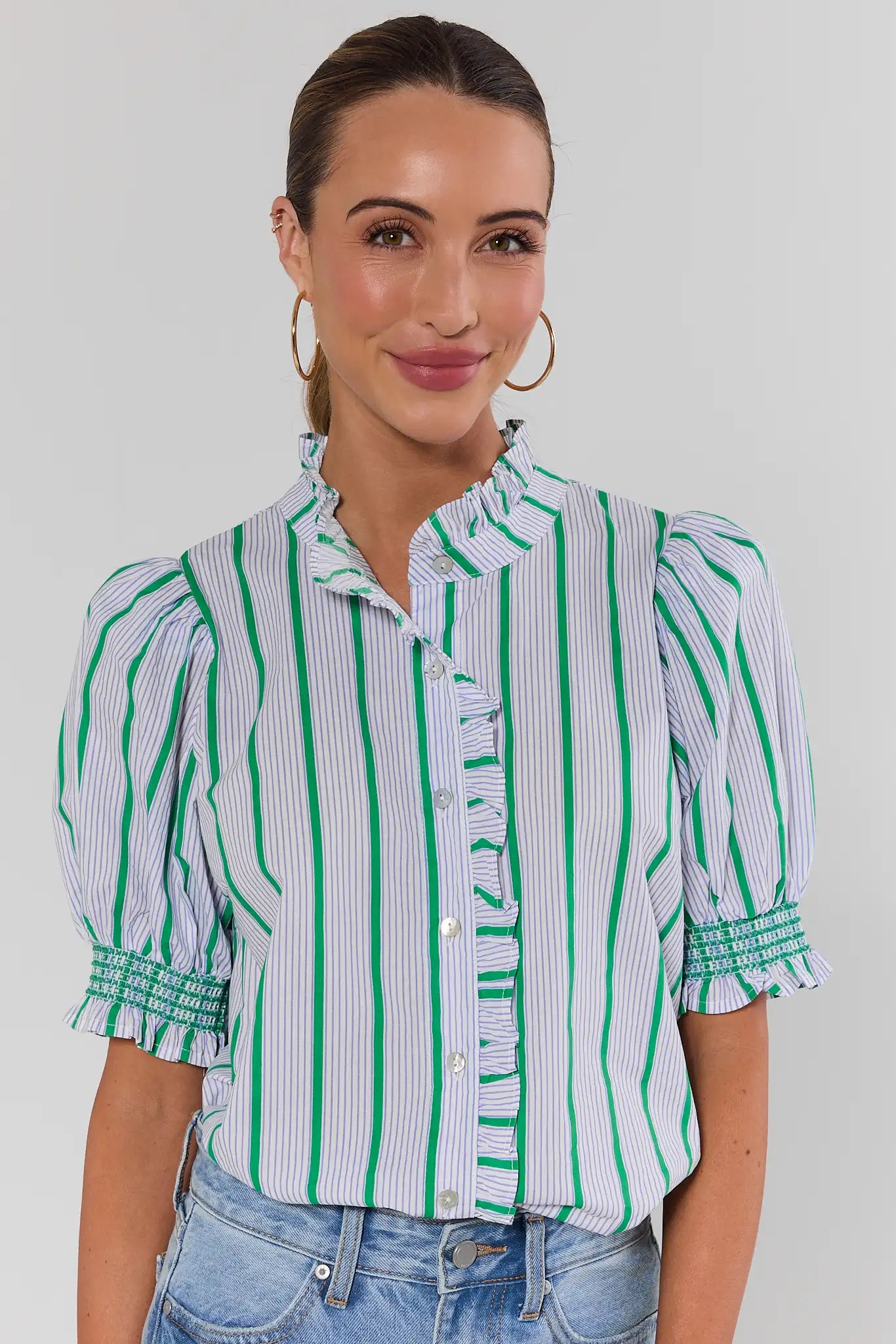 woman standing wearing blue striped ruffle button up top on white background
