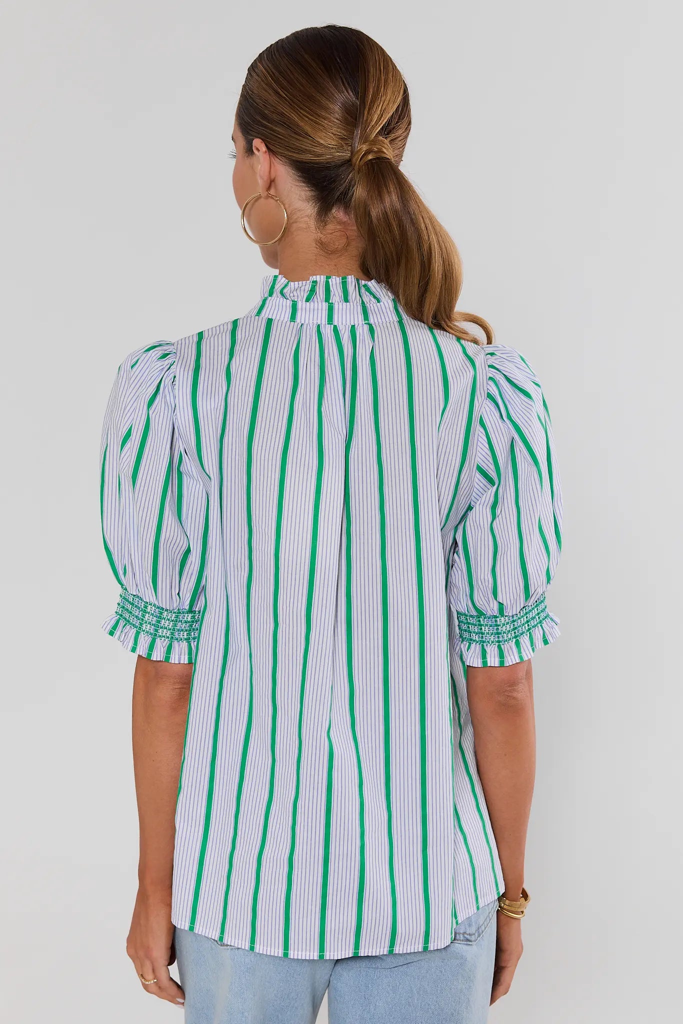 woman wearing blue striped ruffle button up top on white background standing