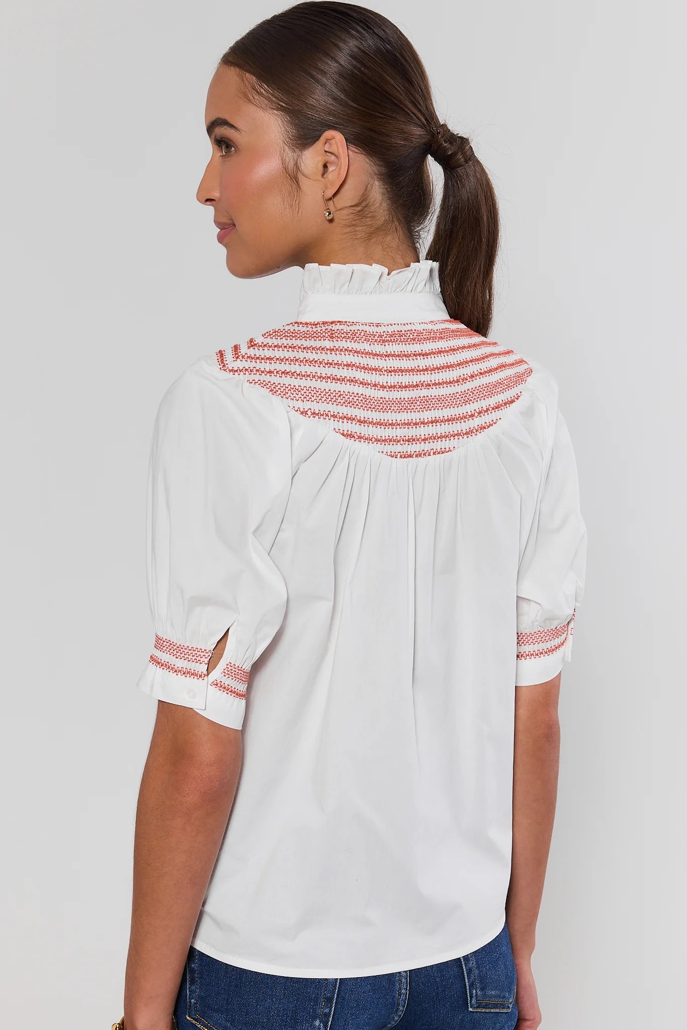 Woman wearing Yvonne White and Orange Embroidered Top on a white background standing