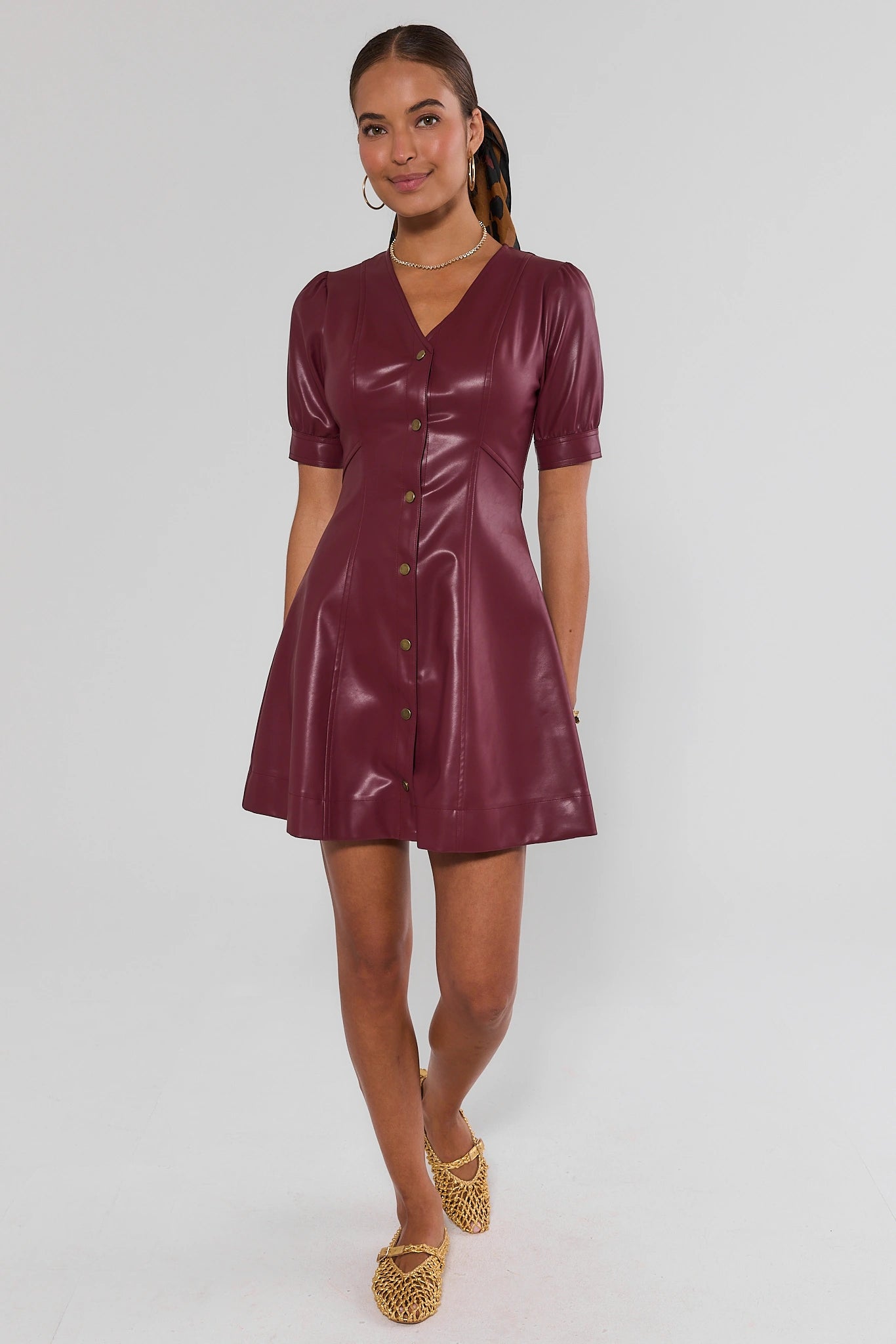 A woman wearing a burgundy short sleeve dress with buttons down the front with gold flats on a white background