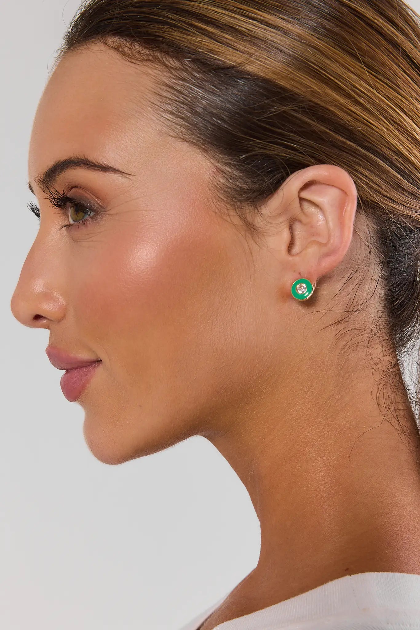 A close-up side profile of a woman wearing a small round stud earring with a green background and a white clover-like emblem.
