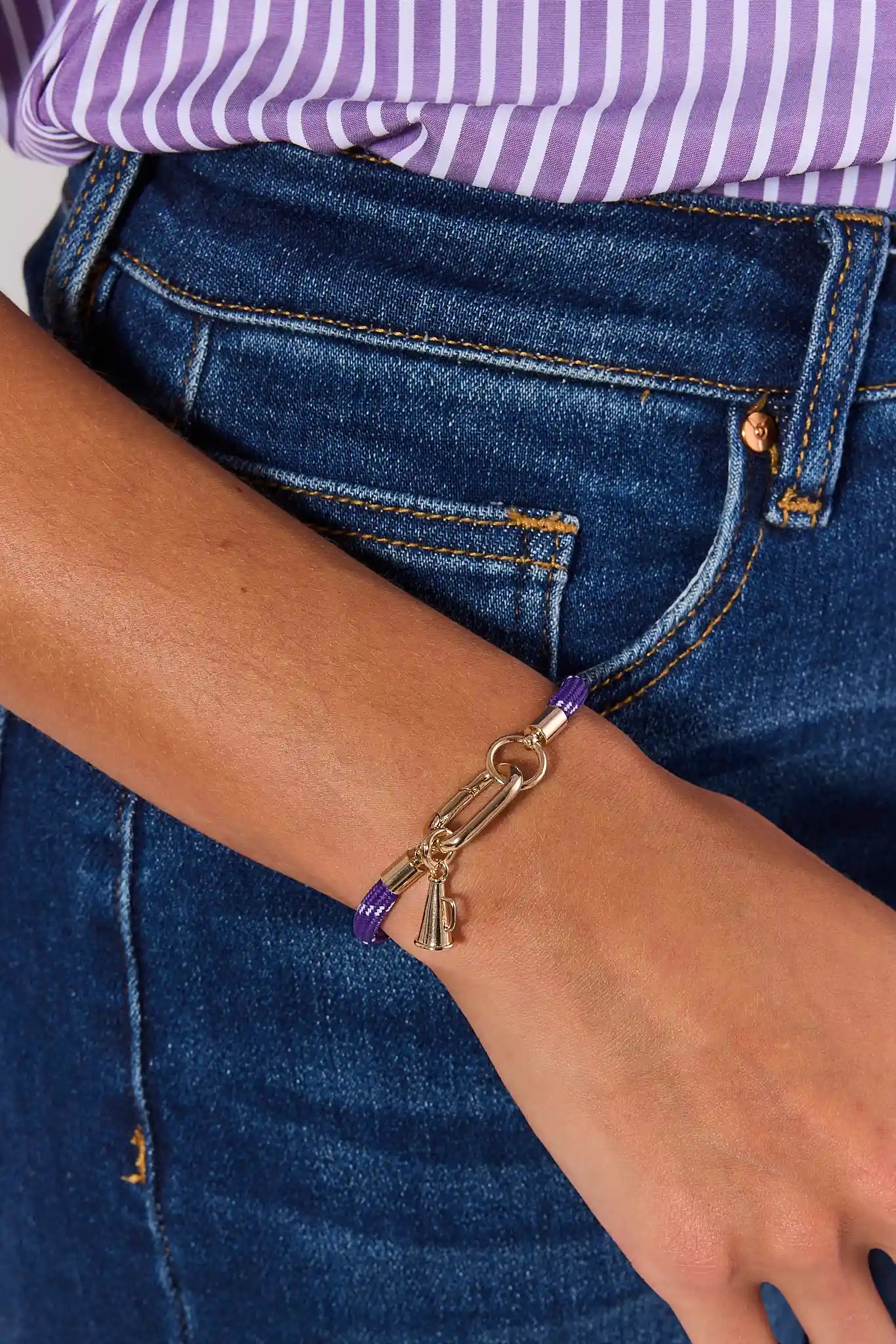 A purple woven rope bracelet with a gold-tone lobster clasp and megaphone charm, displayed on a neutral light gray background.