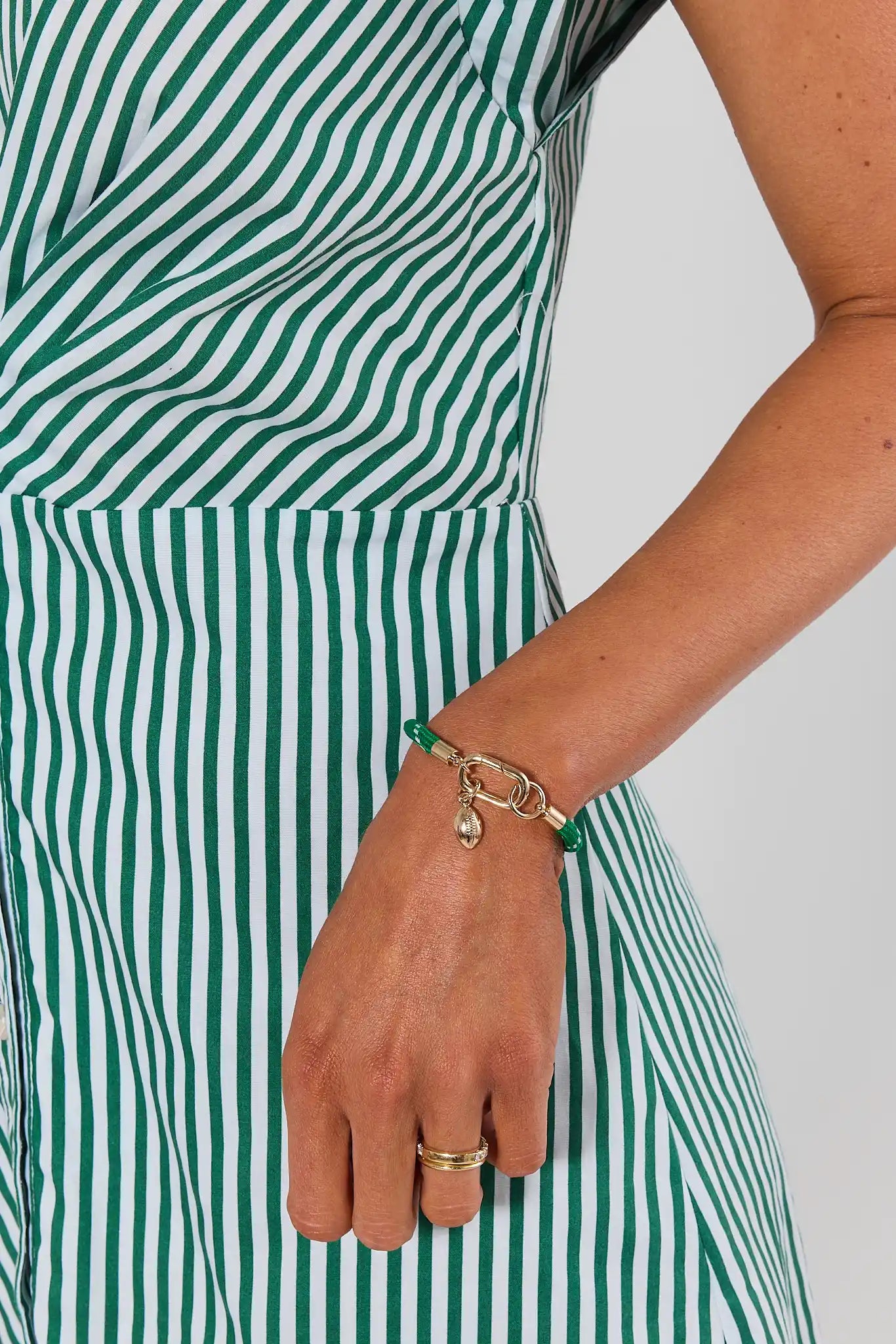A woman wearing a green woven rope bracelet with a gold-tone lobster clasp, with gold charm displayed on a neutral light gray background.