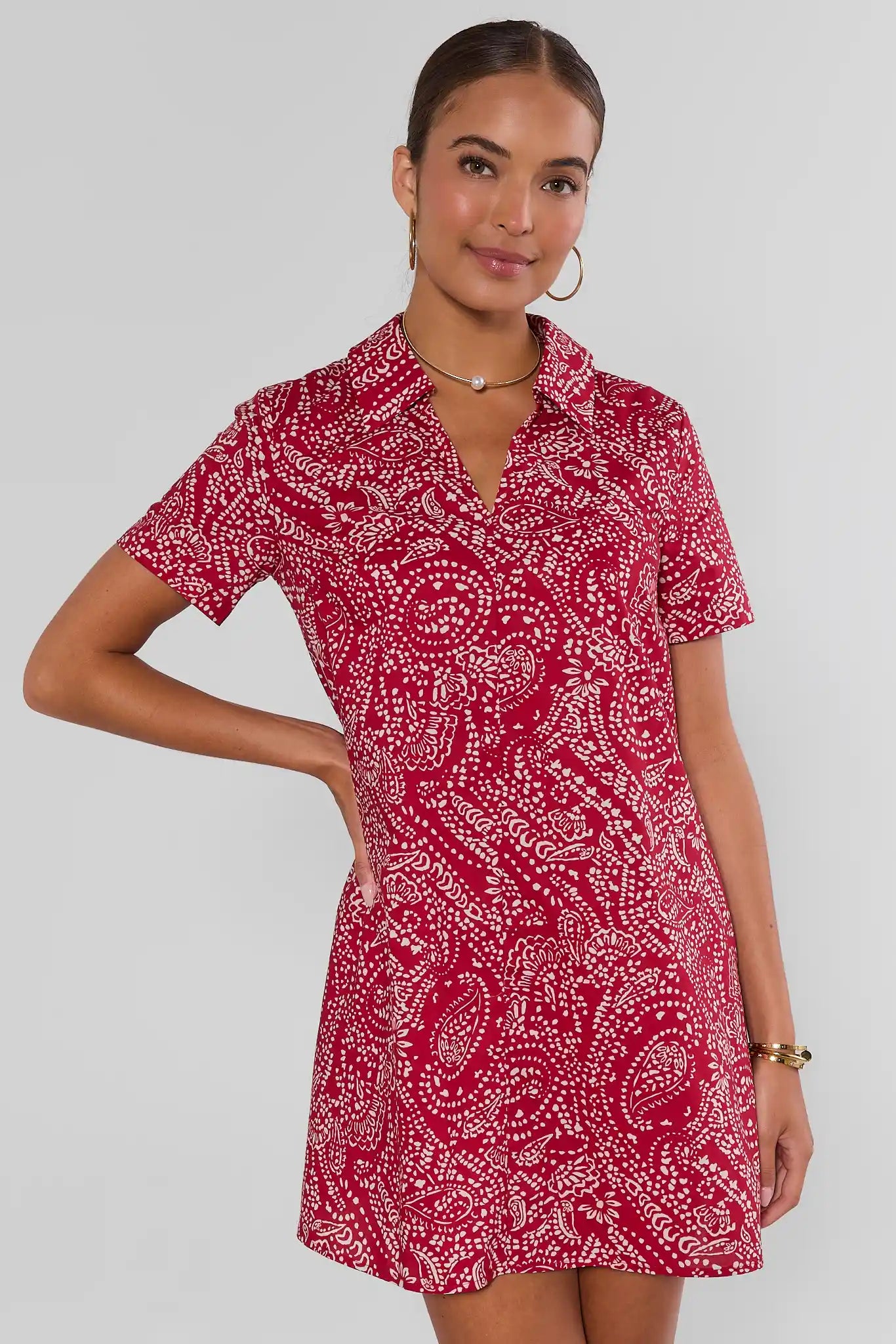 A woman modeling a short-sleeve collared mini dress with a red and white paisley pattern, set against a plain light gray studio background.