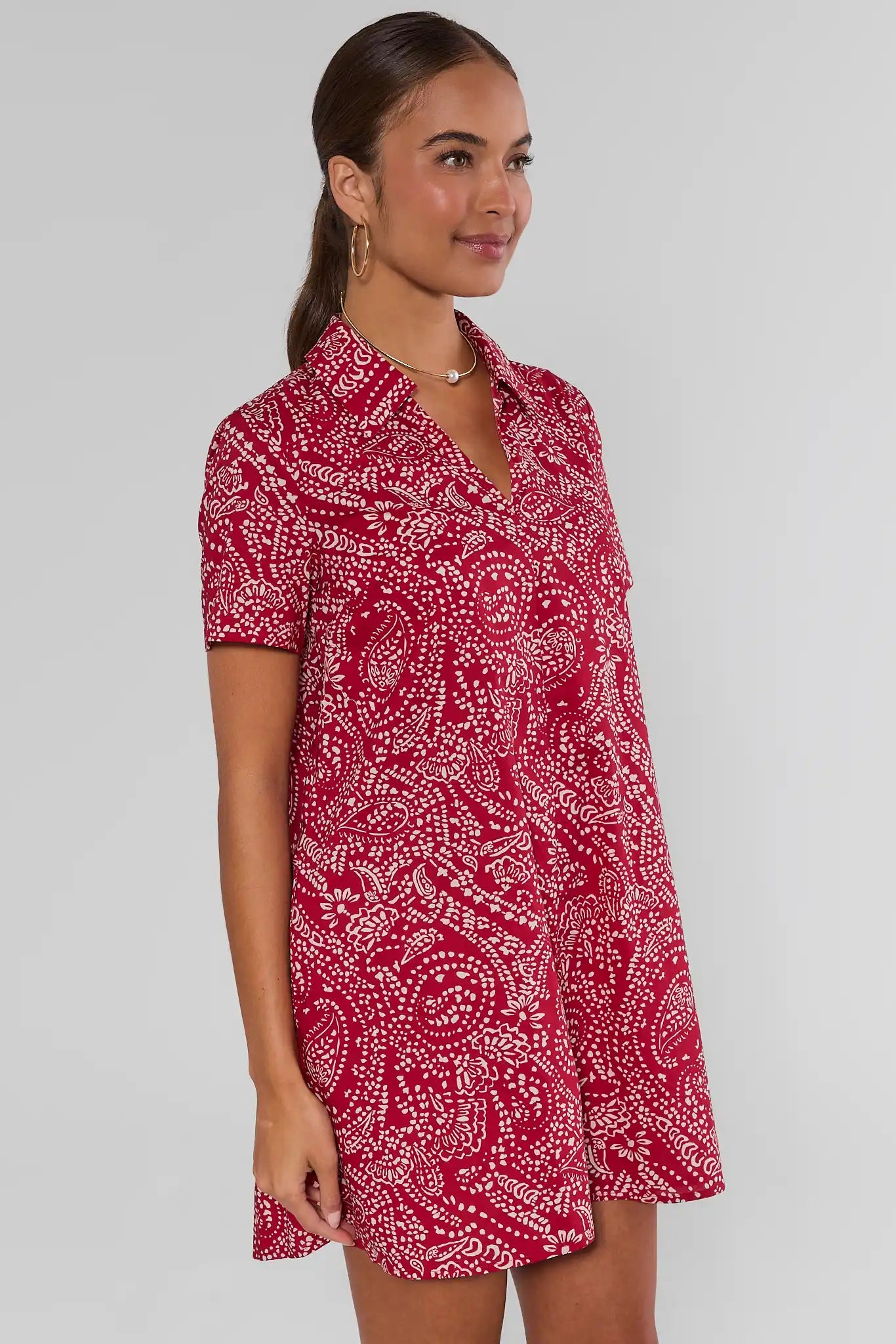 A woman modeling a short-sleeve collared shirt dress with a red and white paisley pattern, photographed against a light studio background.