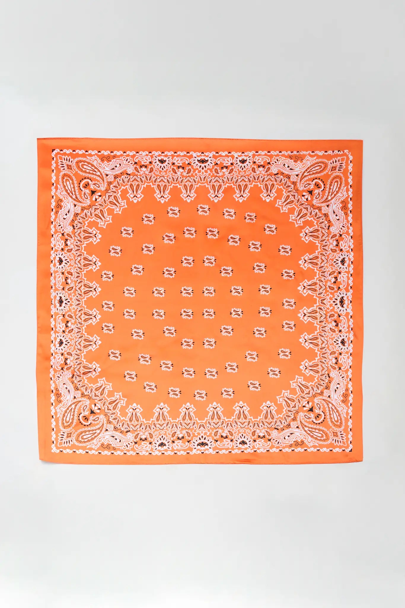 An orange bandana with a white paisley border and a central circular pattern of small white motifs, laid flat against a light gray background.