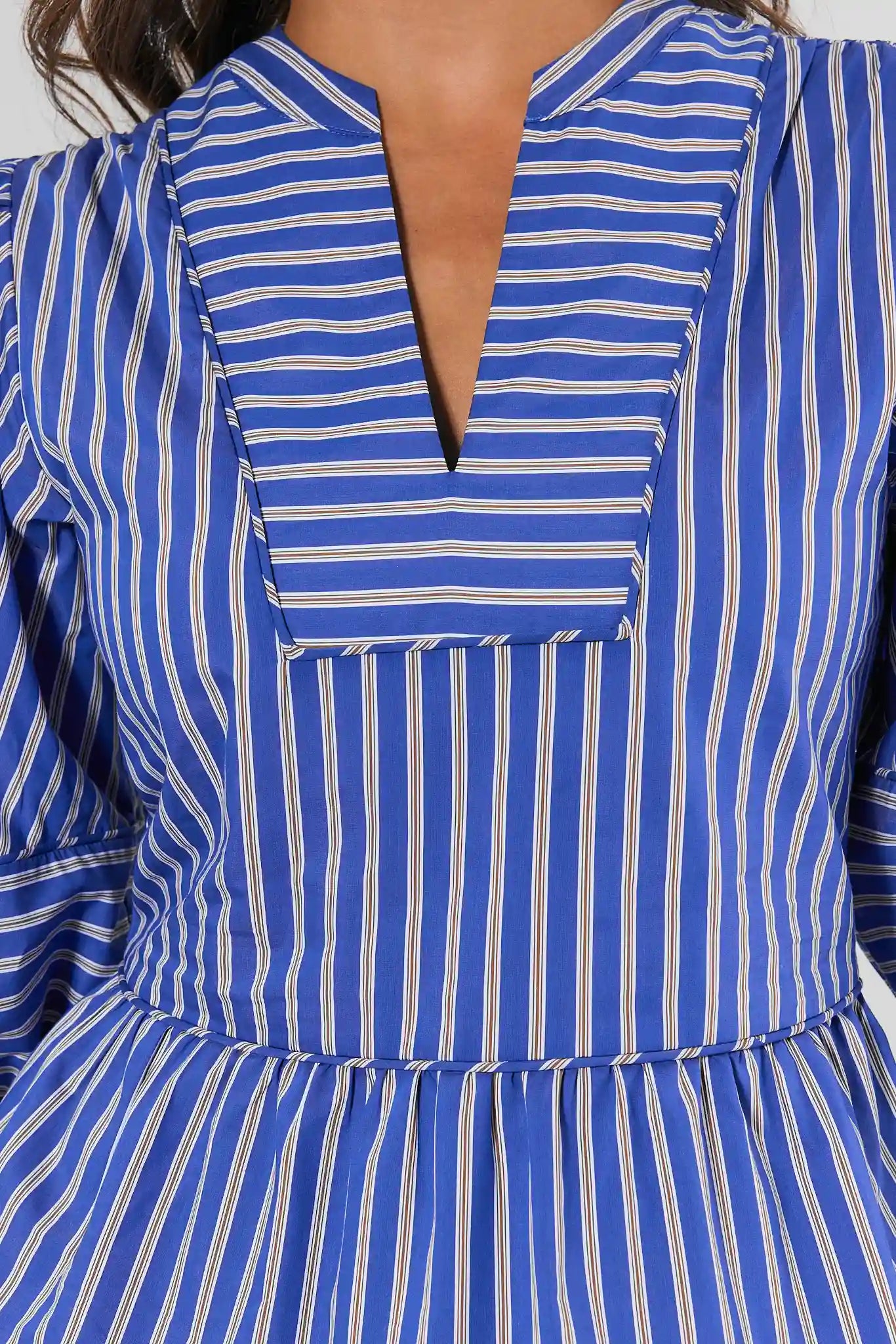 Close-up of a blue and white vertically striped top with a split V-neckline and long sleeves.