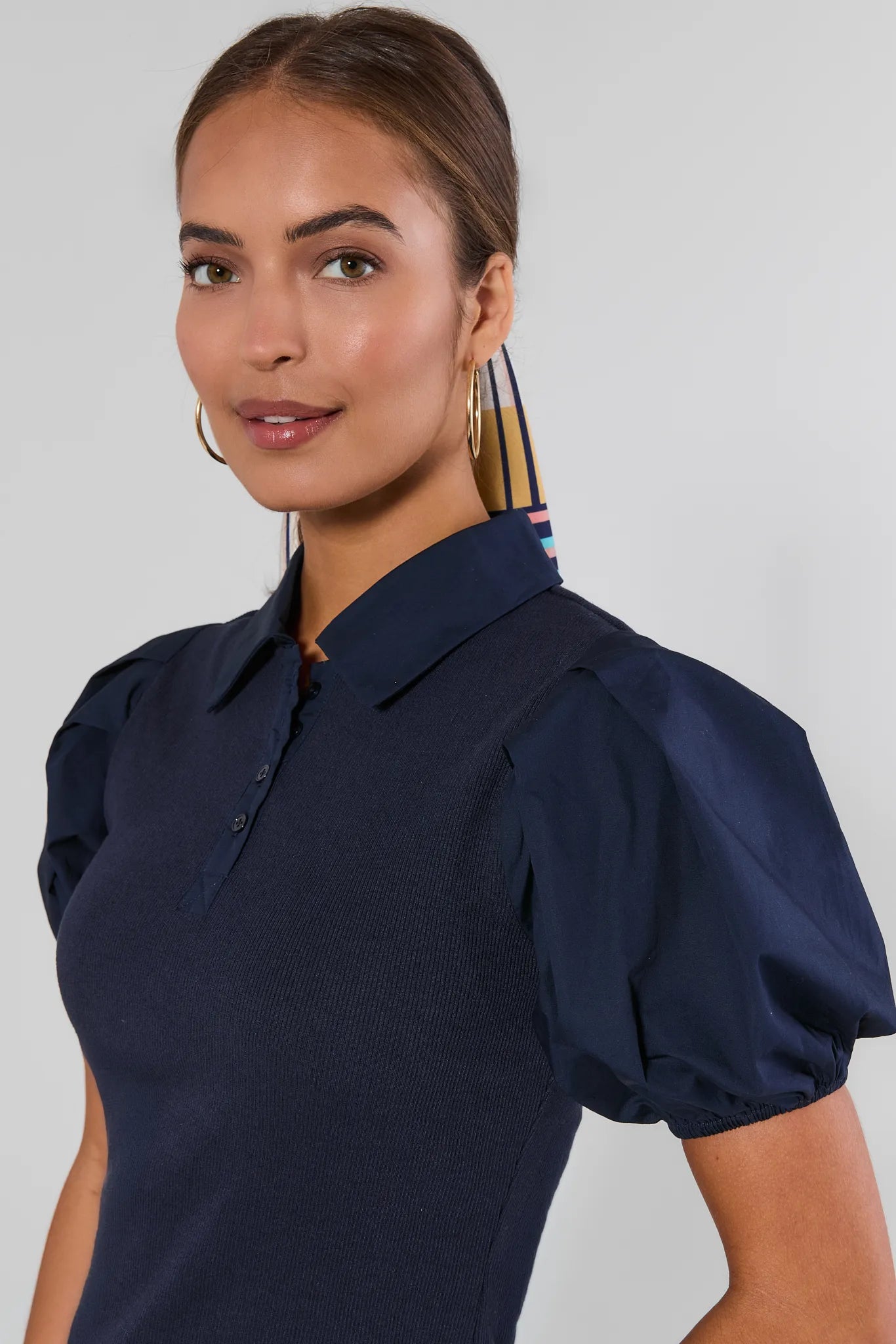 A woman wearing a navy blue short-sleeve polo shirt with puffed sleeves, shown from the chest up against a light gray studio background.