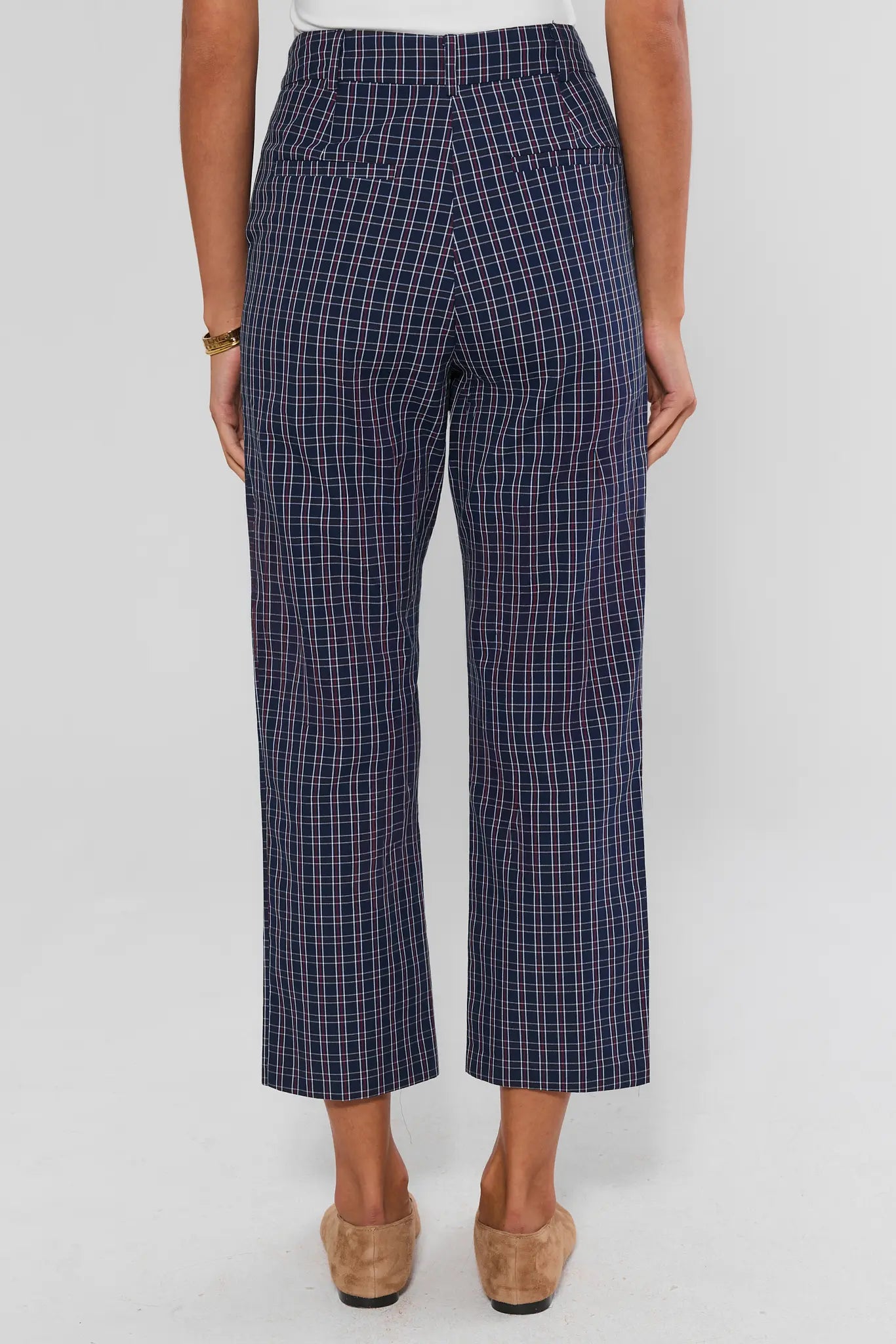 A person shown from the back wearing navy plaid cropped pants with a white top and tan shoes, against a light gray studio background.