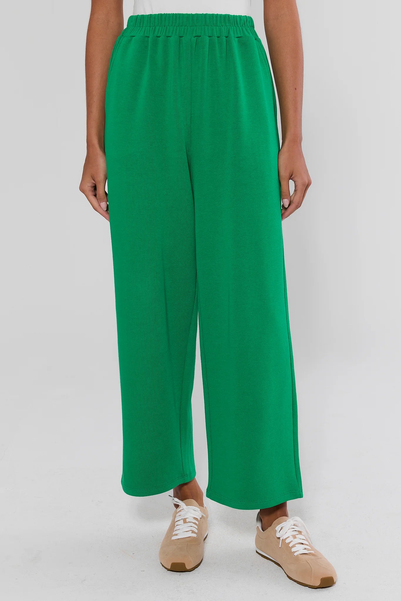 A person wearing bright green wide-leg cropped pants with an elastic waistband, paired with beige sneakers, shown against a plain light gray studio background.
