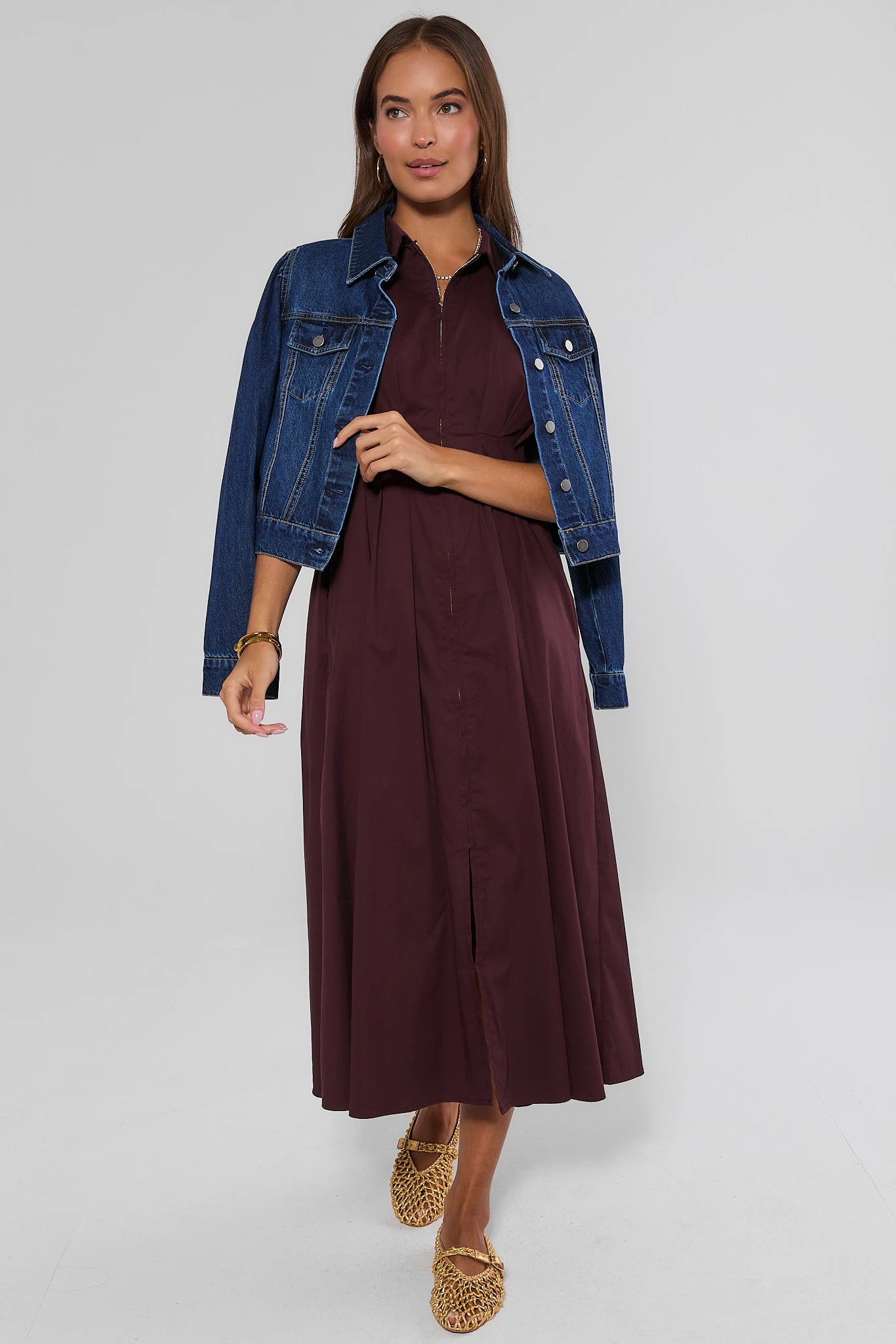 A woman modeling a dark burgundy midi dress with a front slit, styled with a cropped blue denim jacket and leopard-print flat shoes, against a light gray studio background.