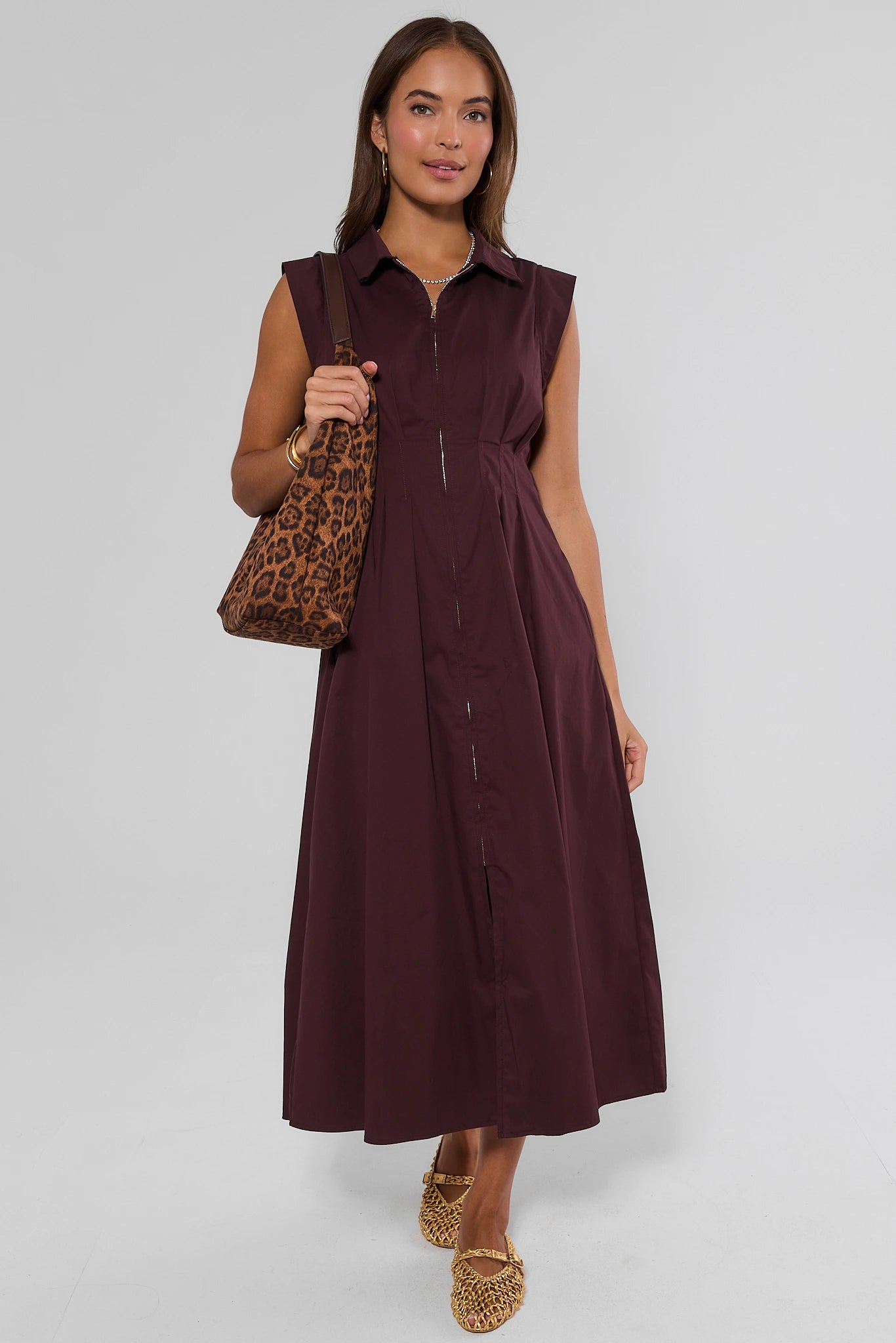 A woman modeling a sleeveless, collared, button-front midi dress in deep burgundy, holding a leopard-print shoulder bag against a light gray studio background.
