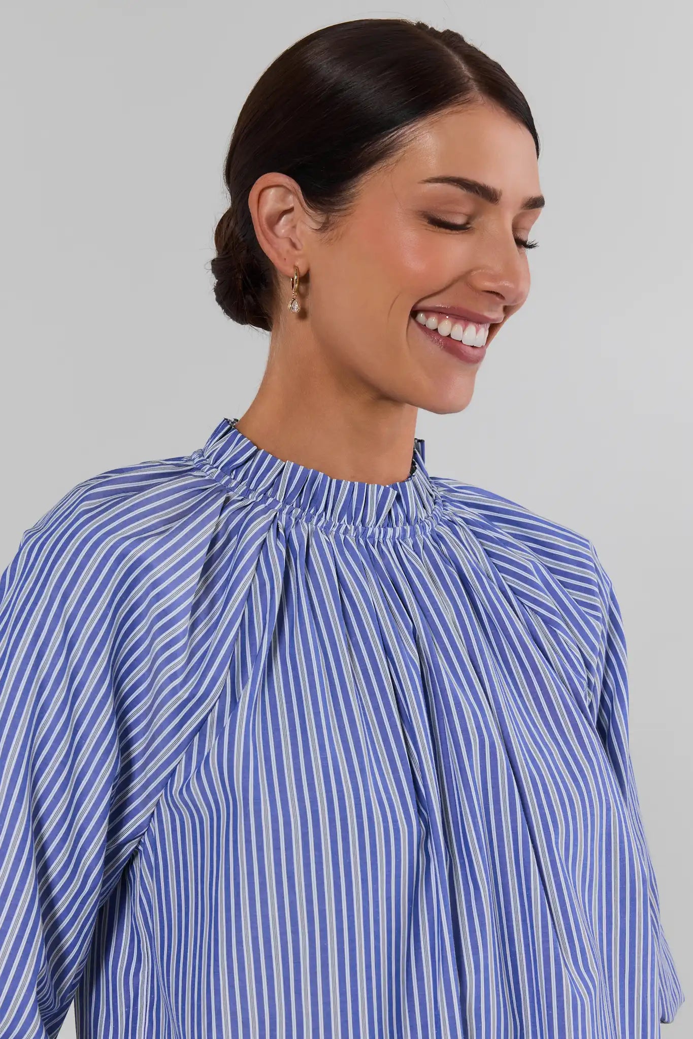 A woman wearing Blue Striped Ruffle Collar Top with a gathered, ruffled high neckline, shown from the chest up against a plain light gray background.