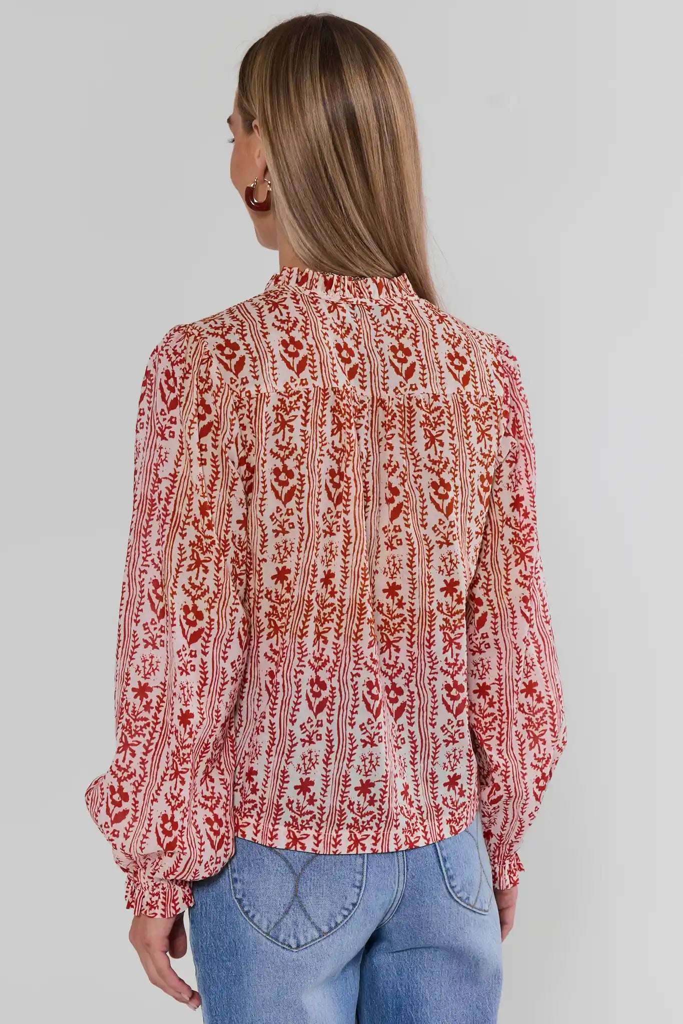 A woman shown from the back wearing a Red Floral Printed Button Up Top paired with blue jeans, against a light gray studio background.