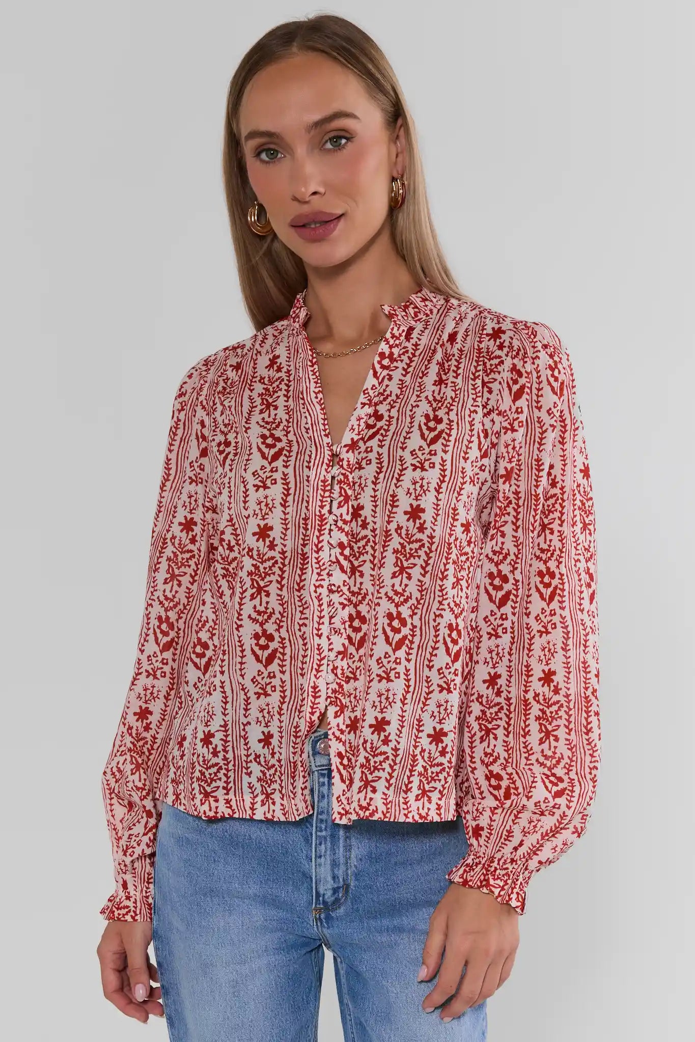 A woman wearing Red Floral Printed Button Up Top paired with blue jeans, against a plain light gray studio background.
