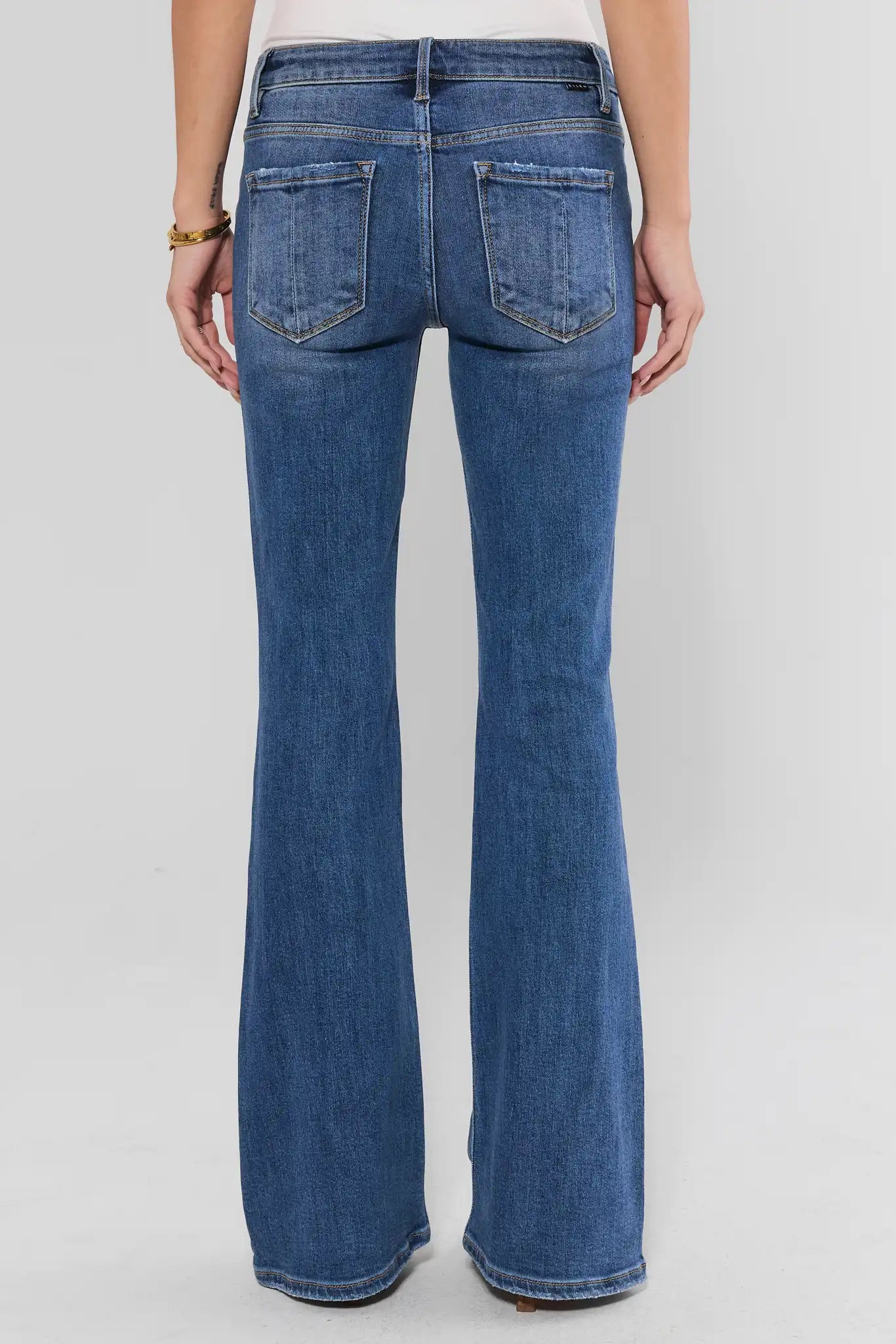Rear view of a person wearing blue denim flare jeans against a light gray studio background.