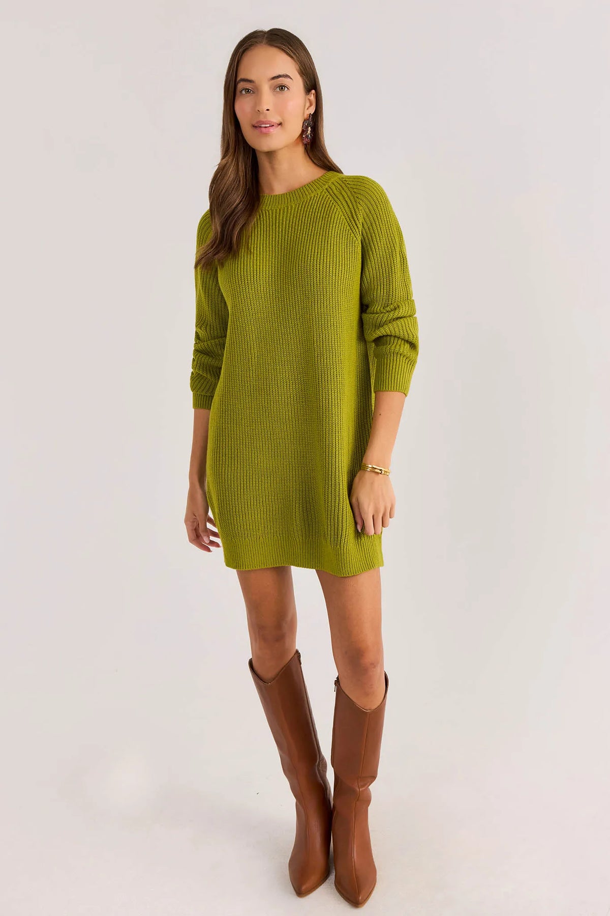 A woman modeling a ribbed knit long-sleeve mini dress in olive green, paired with brown knee-high boots, against a plain light gray studio background.