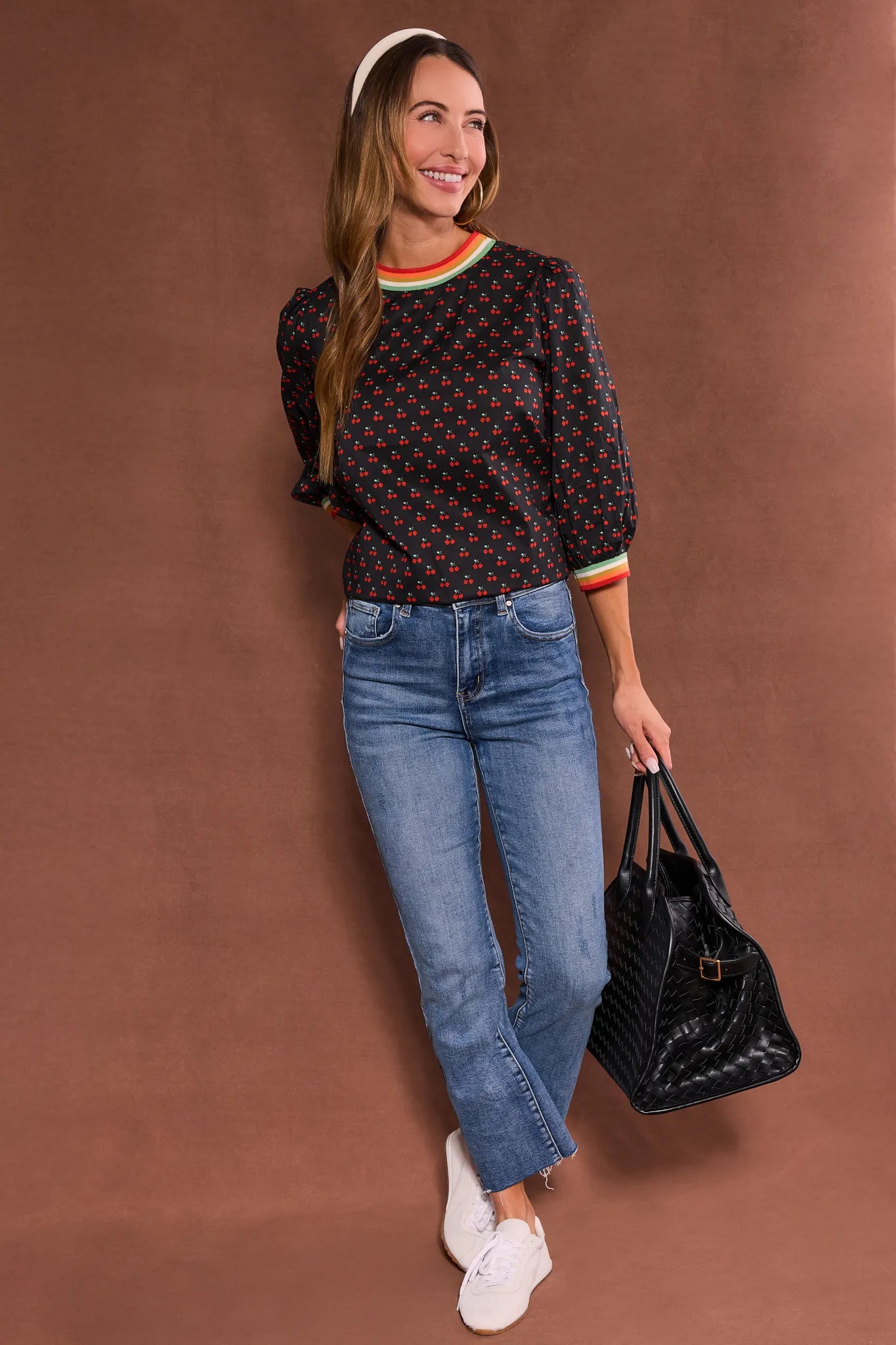 Woman wearing a patterned Bailey Top
 and jeans, holding a black handbag against a brown background