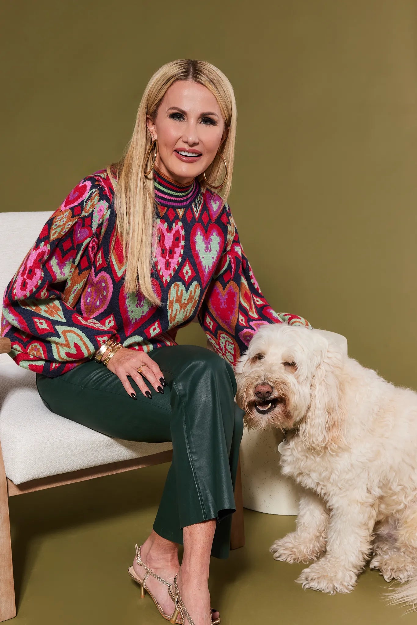 Woman in a colorful Maddie sweater sitting next to a white dog on a green floor.