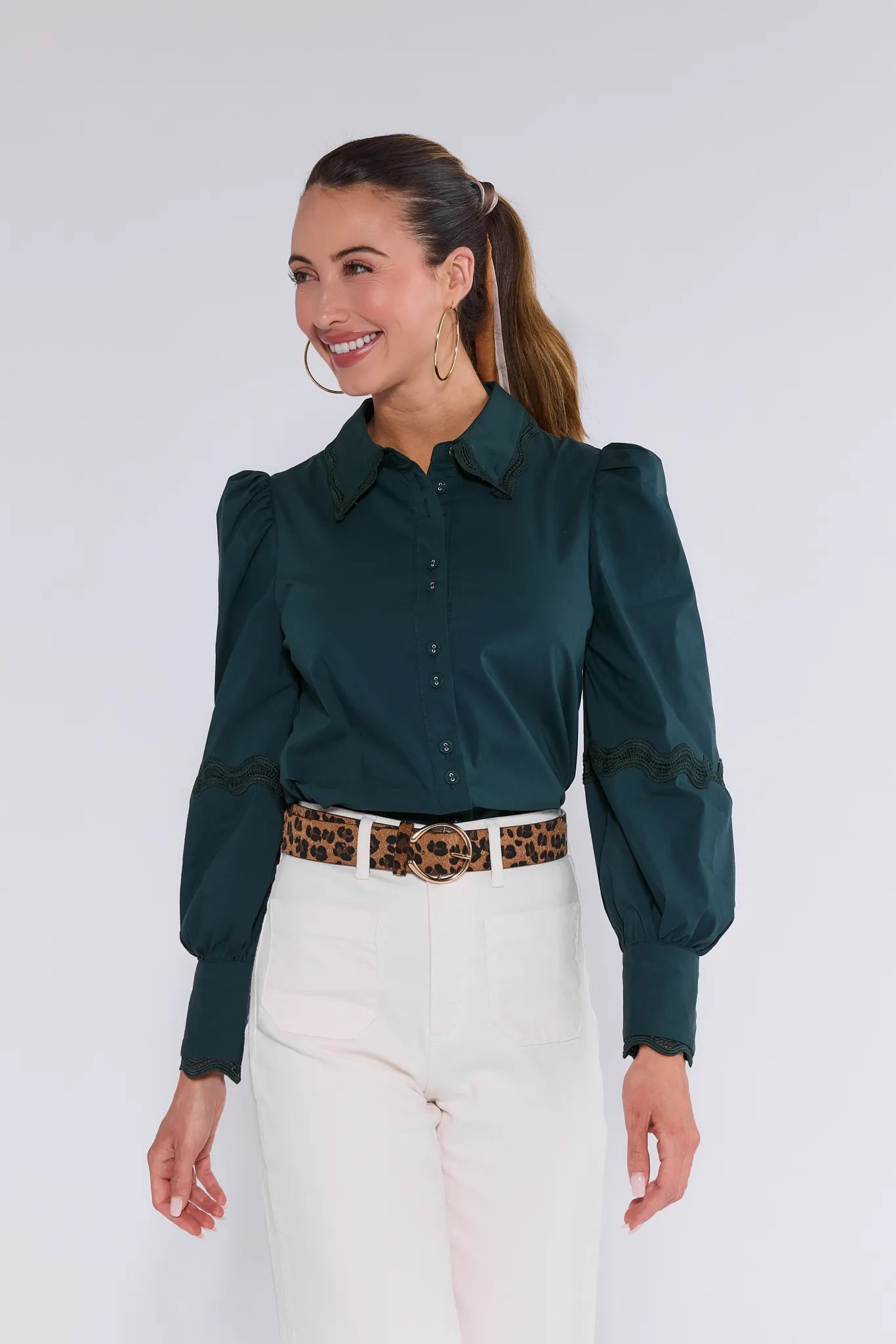 Woman wearing a dark green Ellis Top with long sleeves and white pants against a plain background