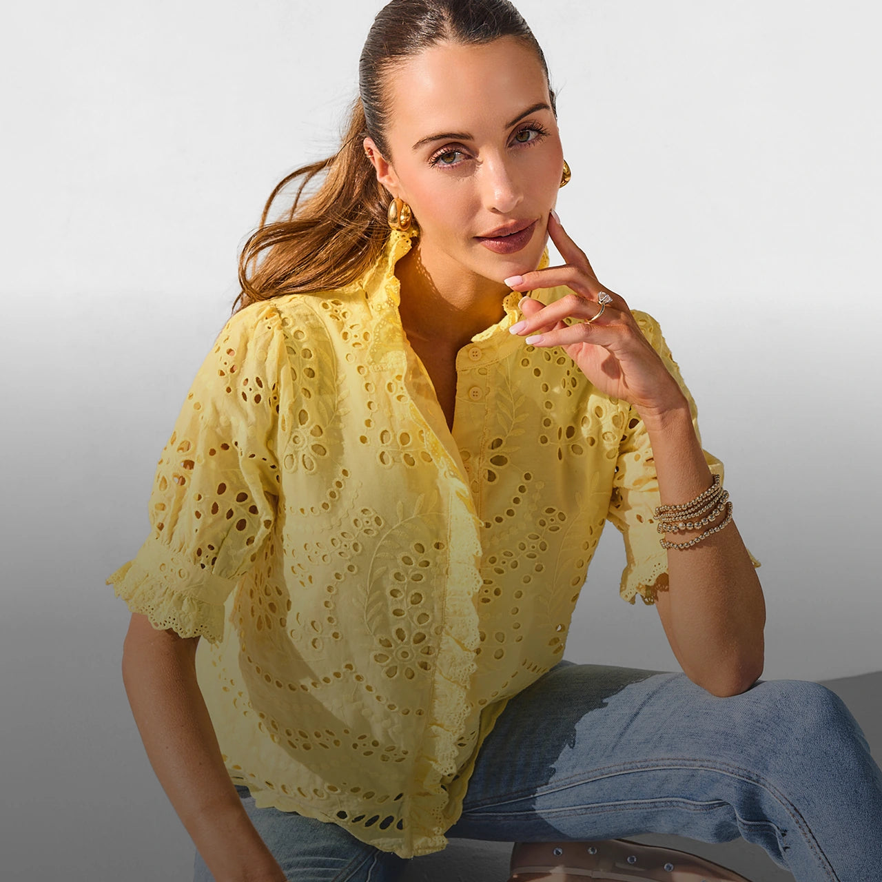 Woman wearing a yellow lace top and blue jeans against a plain background