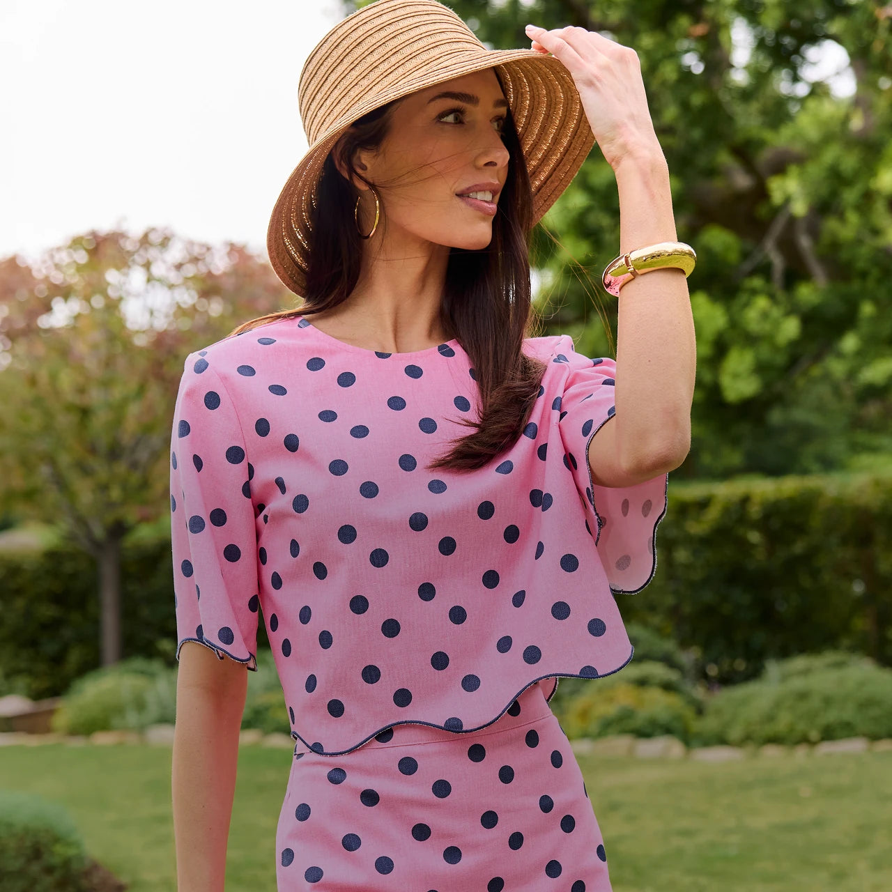 Woman wearing a pink polka dot dress and straw hat outdoors