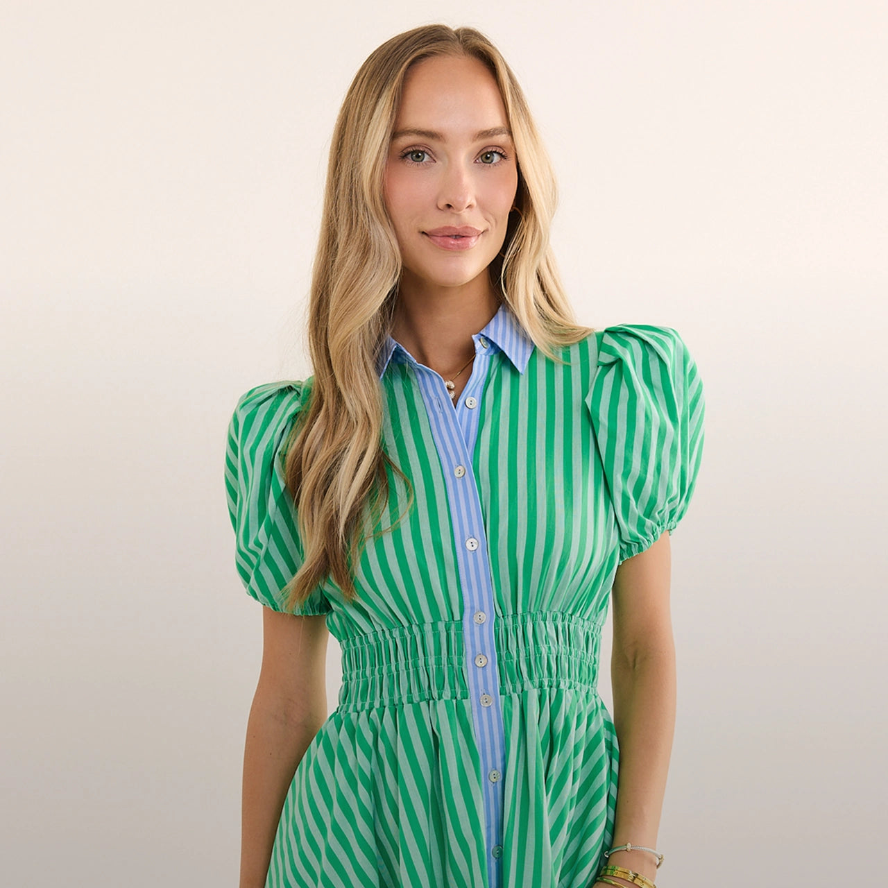 Woman wearing a green and white striped dress with a plain background hero