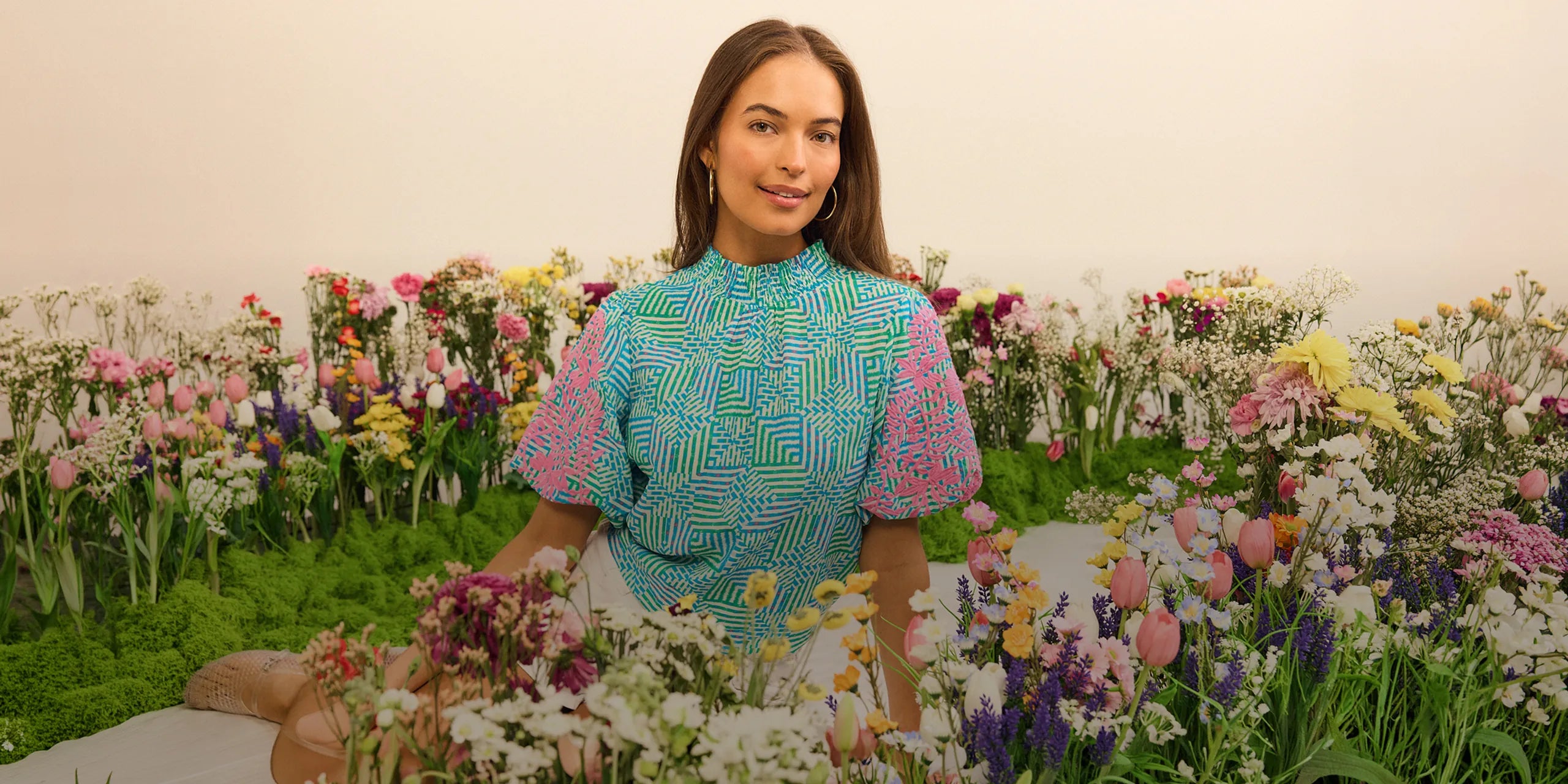 Woman in a colorful outfit standing among flowers with a neutral background