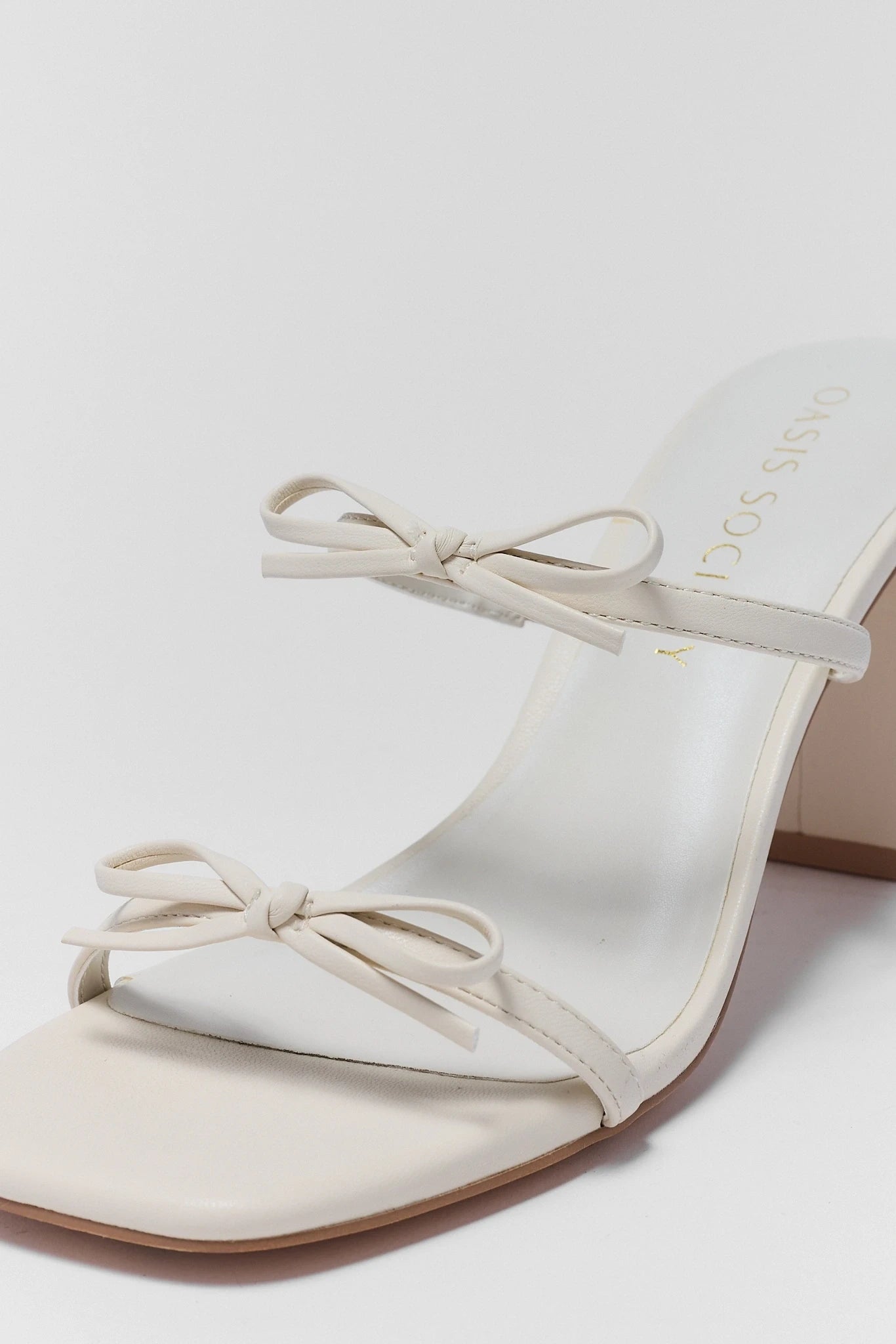 White sandal with clear heel and bow detail on a light background