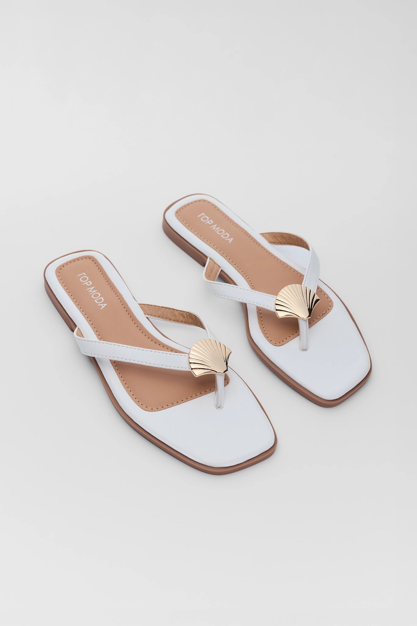 Pair of white sandals with gold shell decorations on a light gray background two