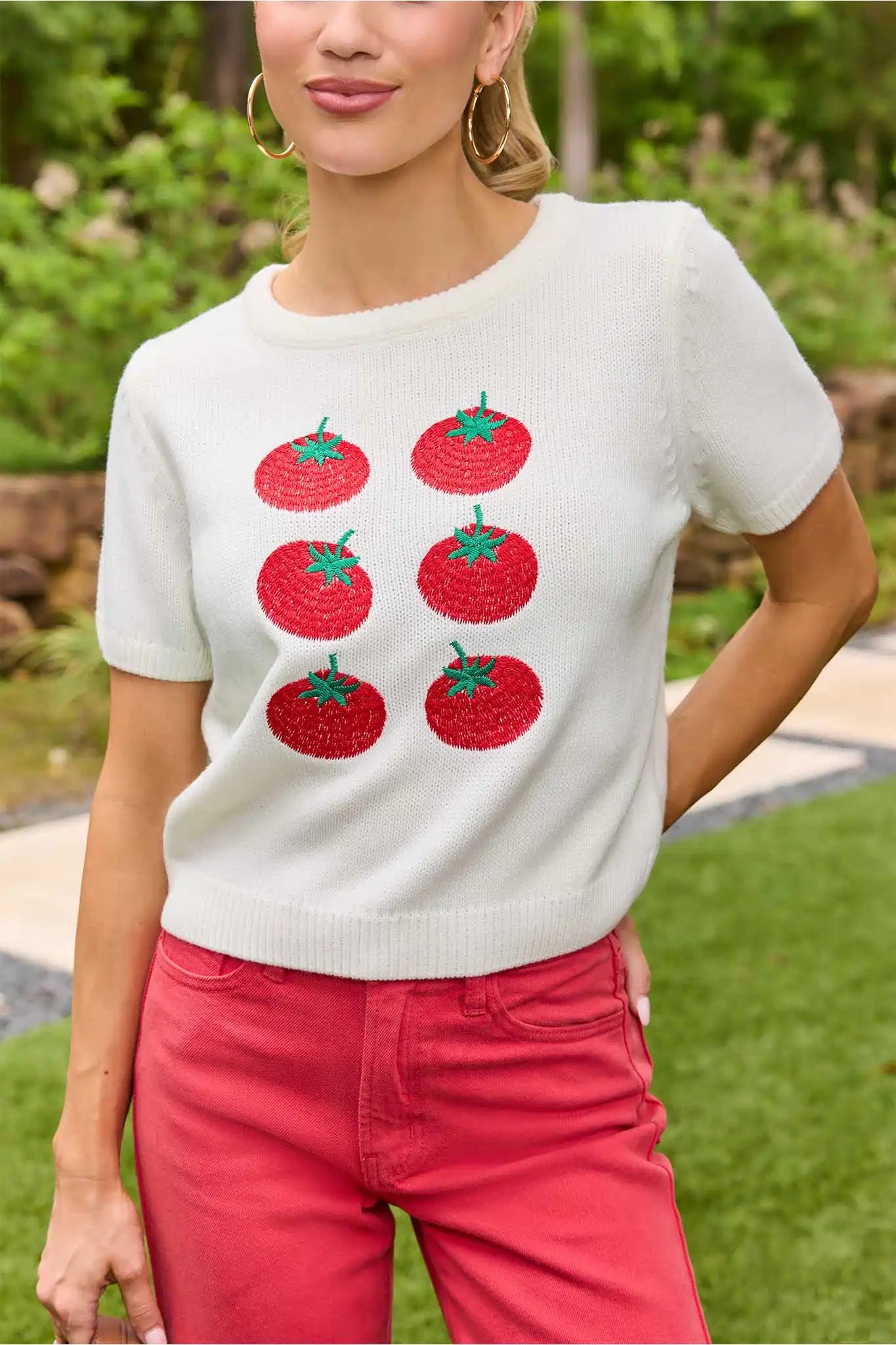 Woman wearing a white sweater with red tomato designs outdoors close up 