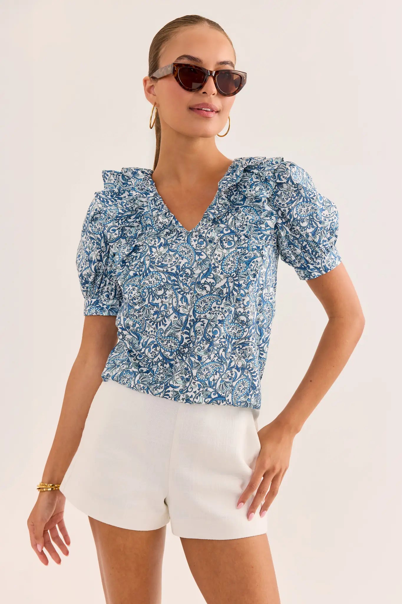Woman wearing a blue floral blouse and white shorts against a plain background