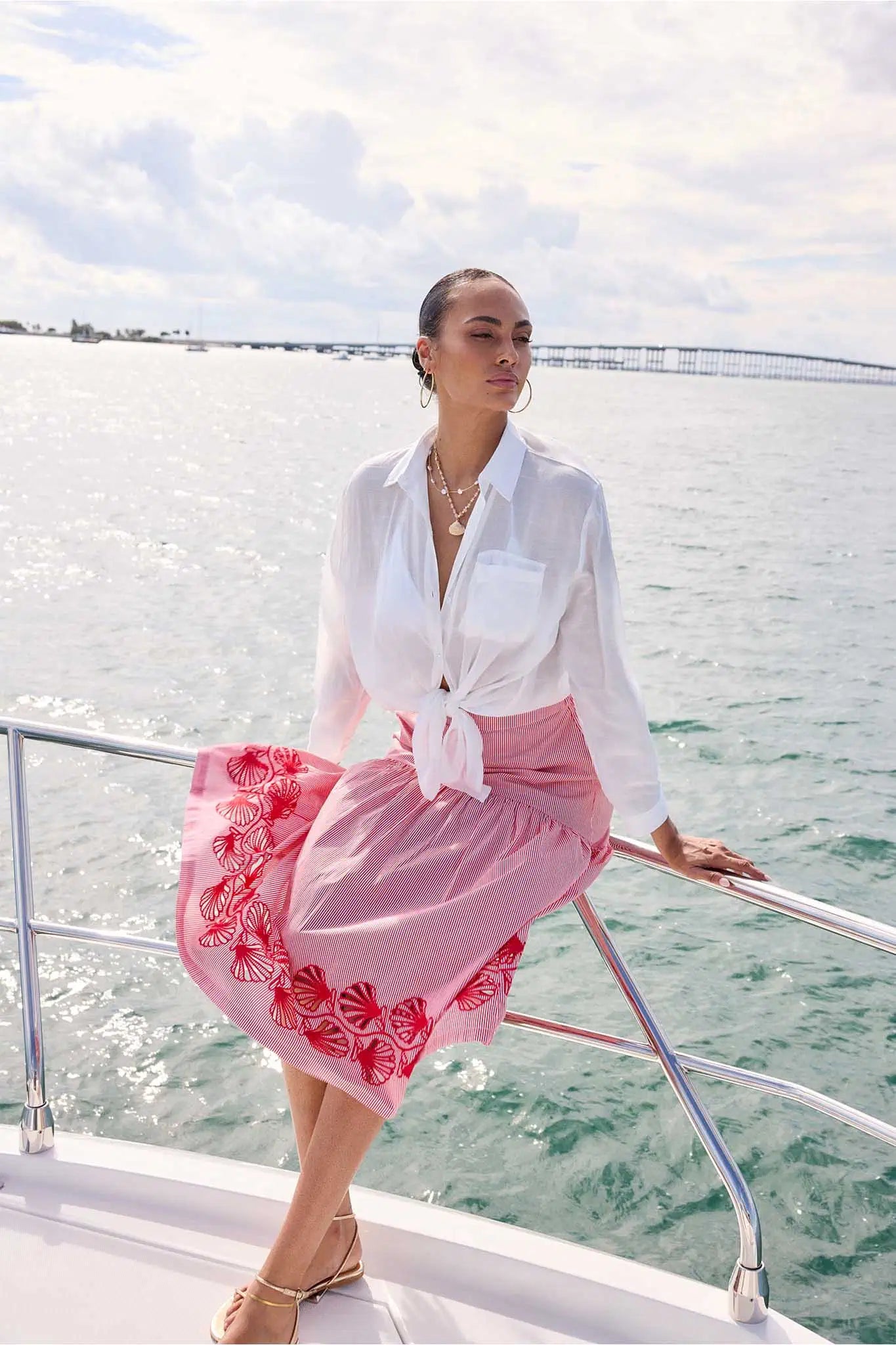 Woman in a white blouse and pink skirt on a boat with water and sky in the background