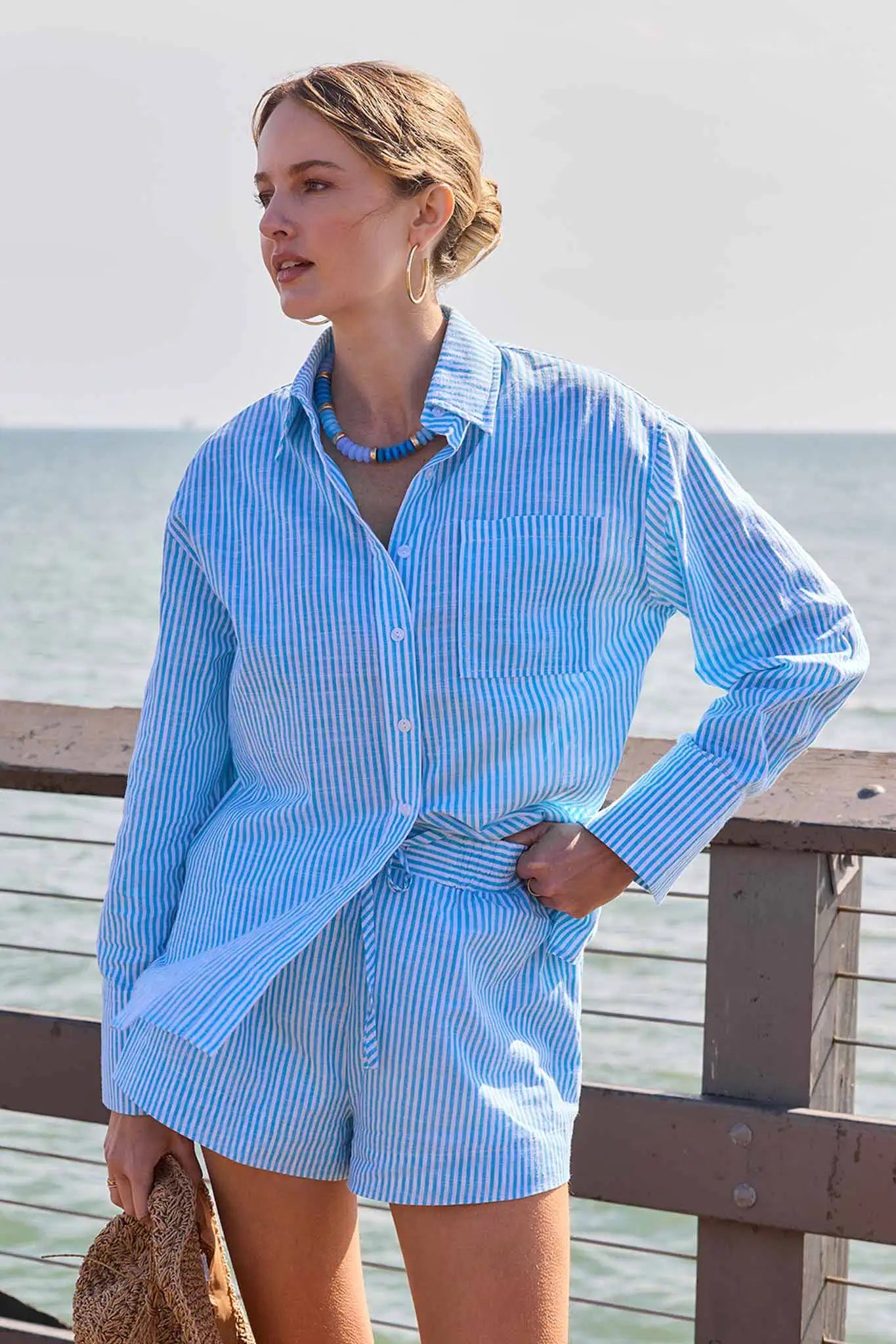 Woman wearing a blue striped shirt and shorts by the ocean.