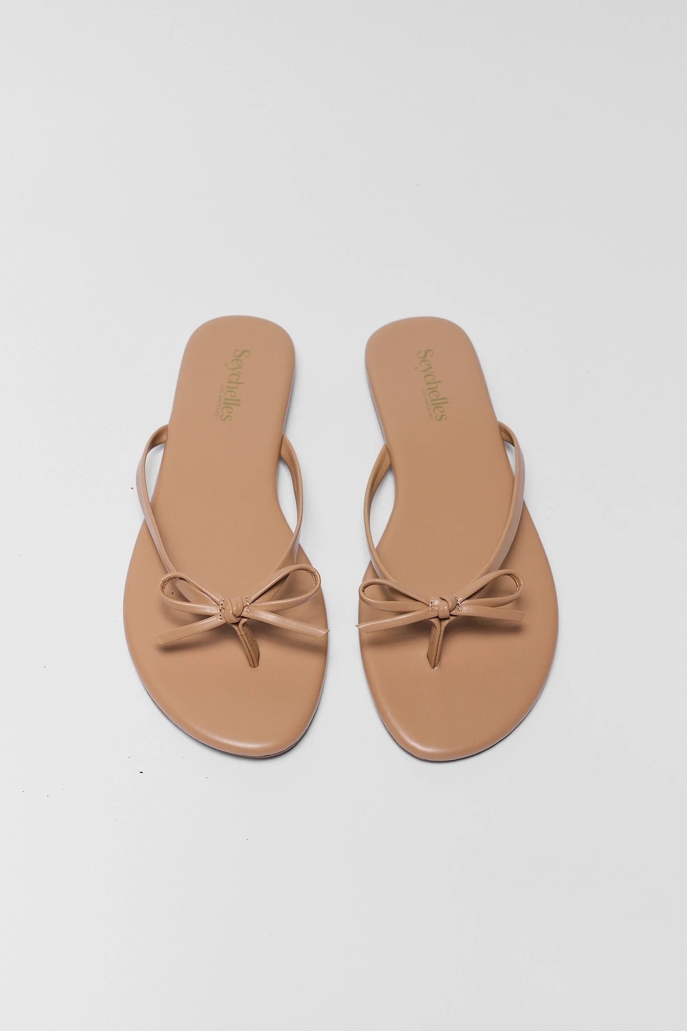 Pair of tan sandals with bow details on a light gray background two