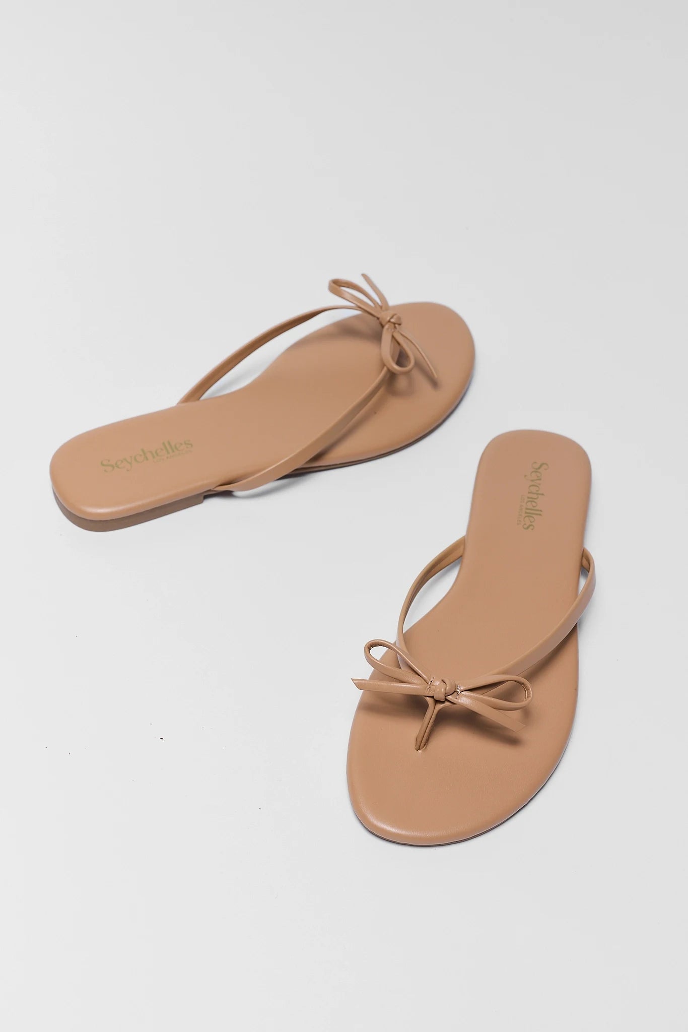 Pair of tan sandals with bow details on a light gray background