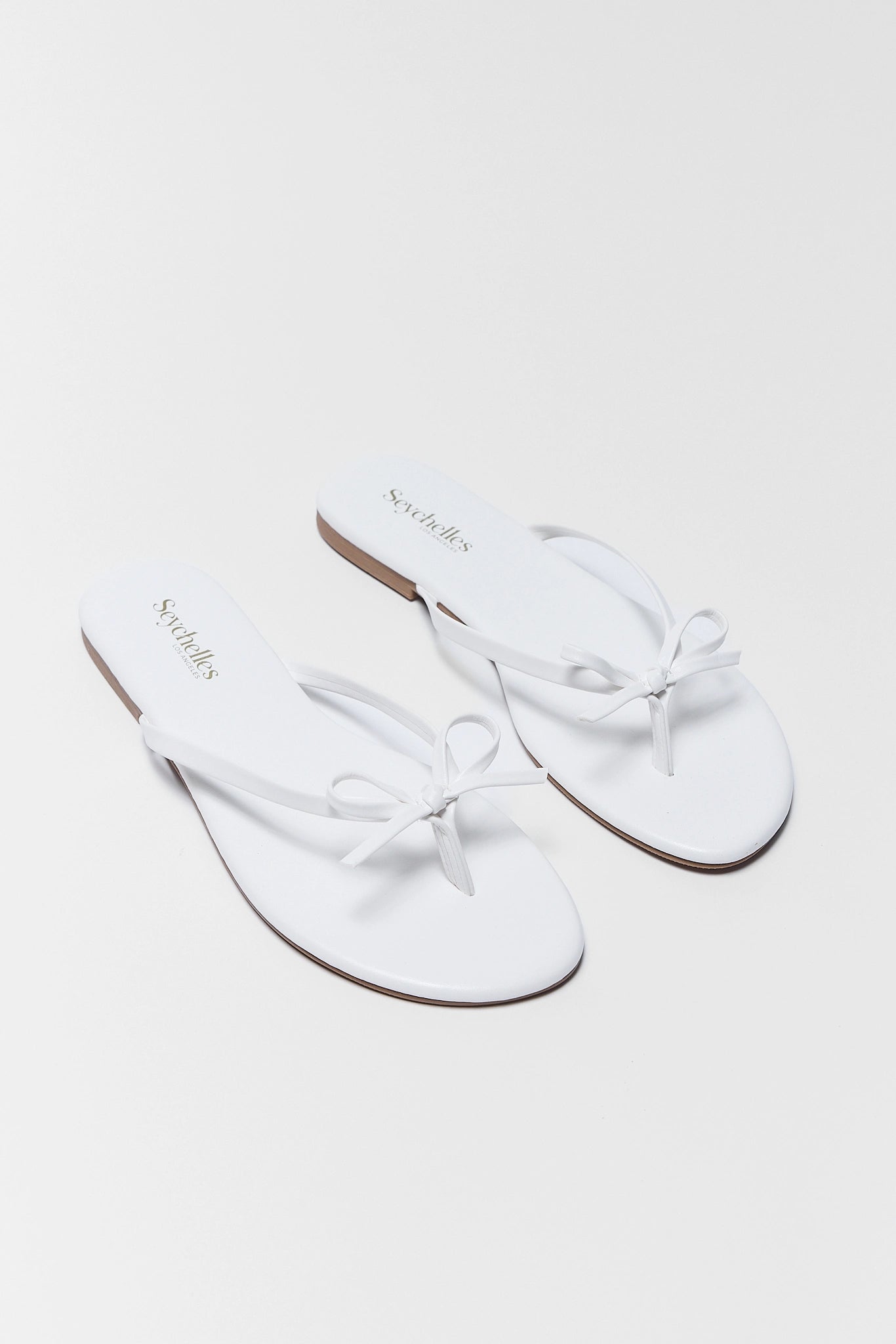 Pair of two white sandals with bow details on a light gray background