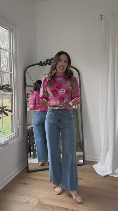 Woman wearing pink short sleeve sweater with blue jeans and mirror in background