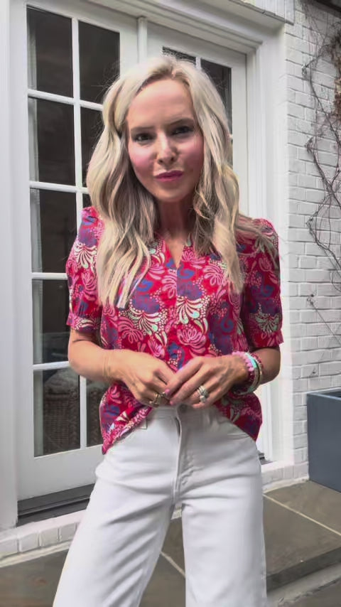 Woman wearing Marilyn Top with puff sleeves and floral print with white jeans standing outside in front of house with door.