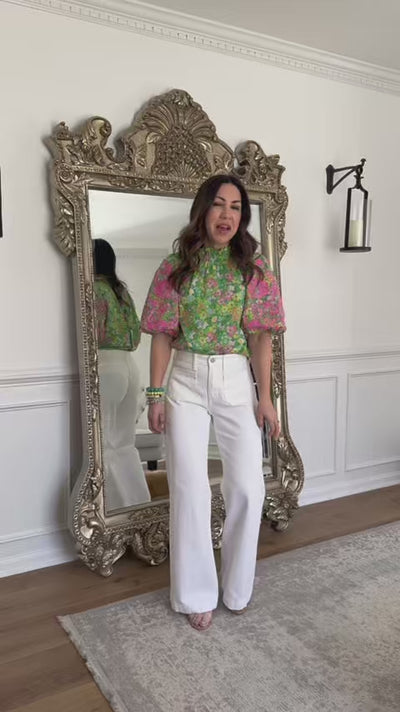 woman wearing green june top with white jeans and mirror in background