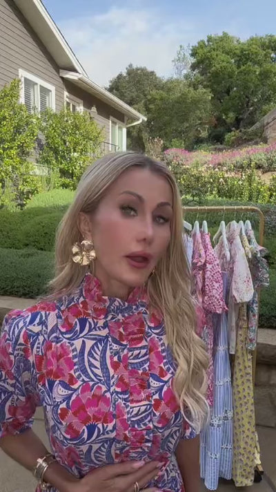Woman wearing pink printed midi dress in front of clothing rack outside 