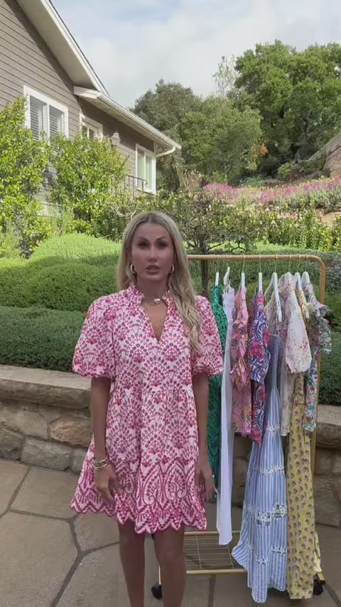 Woman in pink embroidered short dress outside in front of clothing rack