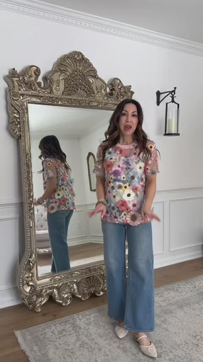 woman wearing floral applique top with jeans standing in front of mirror