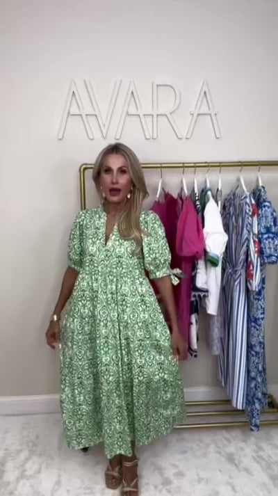 woman wearing a green midi dress Harriet with a rack of clothing behind her